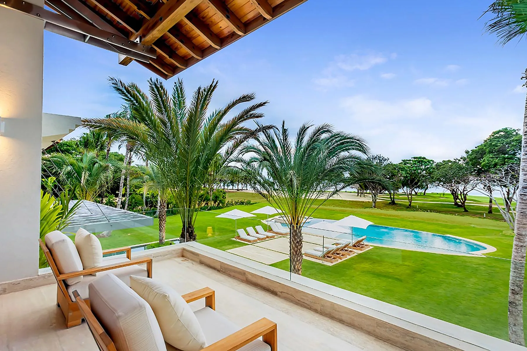 Un patio cubierto da a palmeras, césped verde y una piscina.