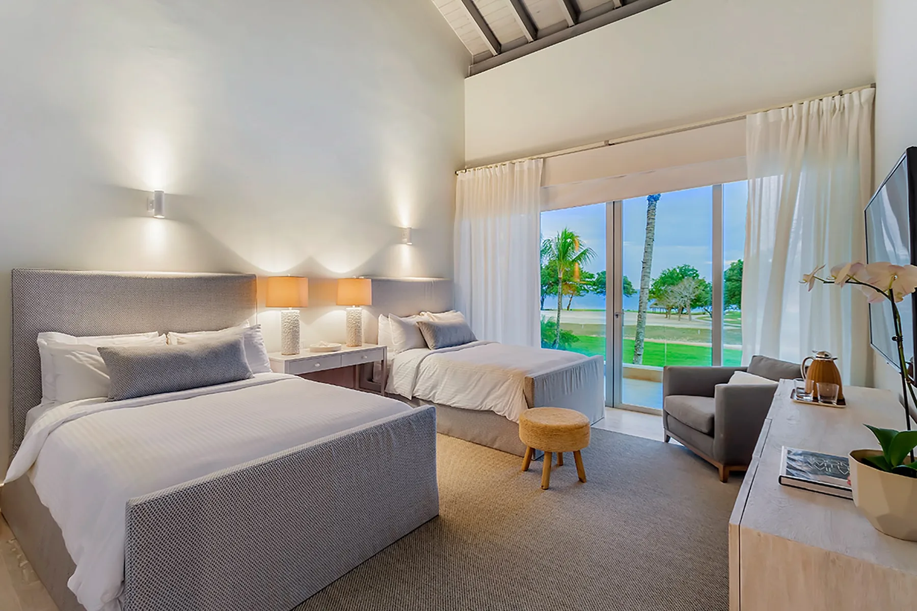 Un dormitorio luminoso con dos camas y puertas corredizas de vidrio que dan a un jardín.