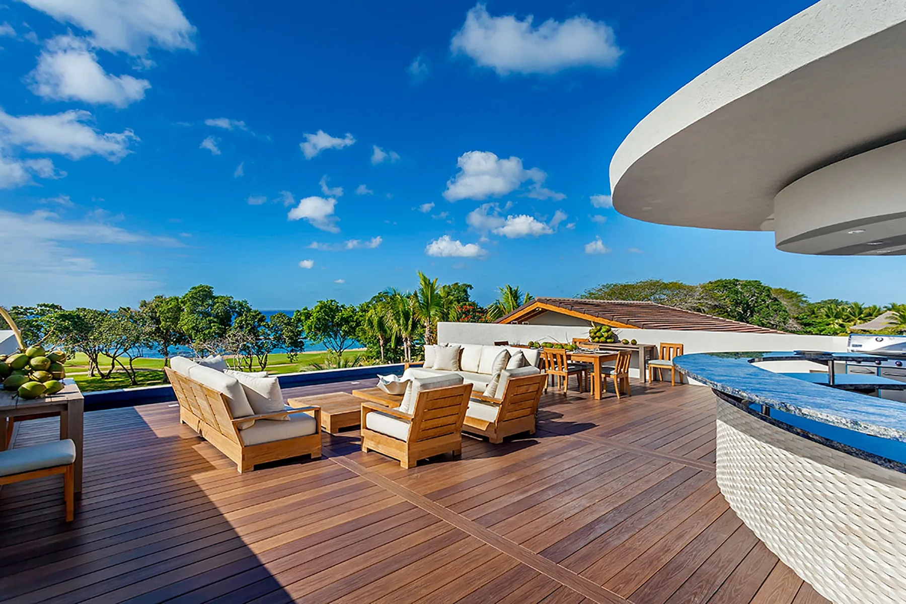 Una terraza exterior tiene asientos de madera junto a una piscina, con vistas al mar.