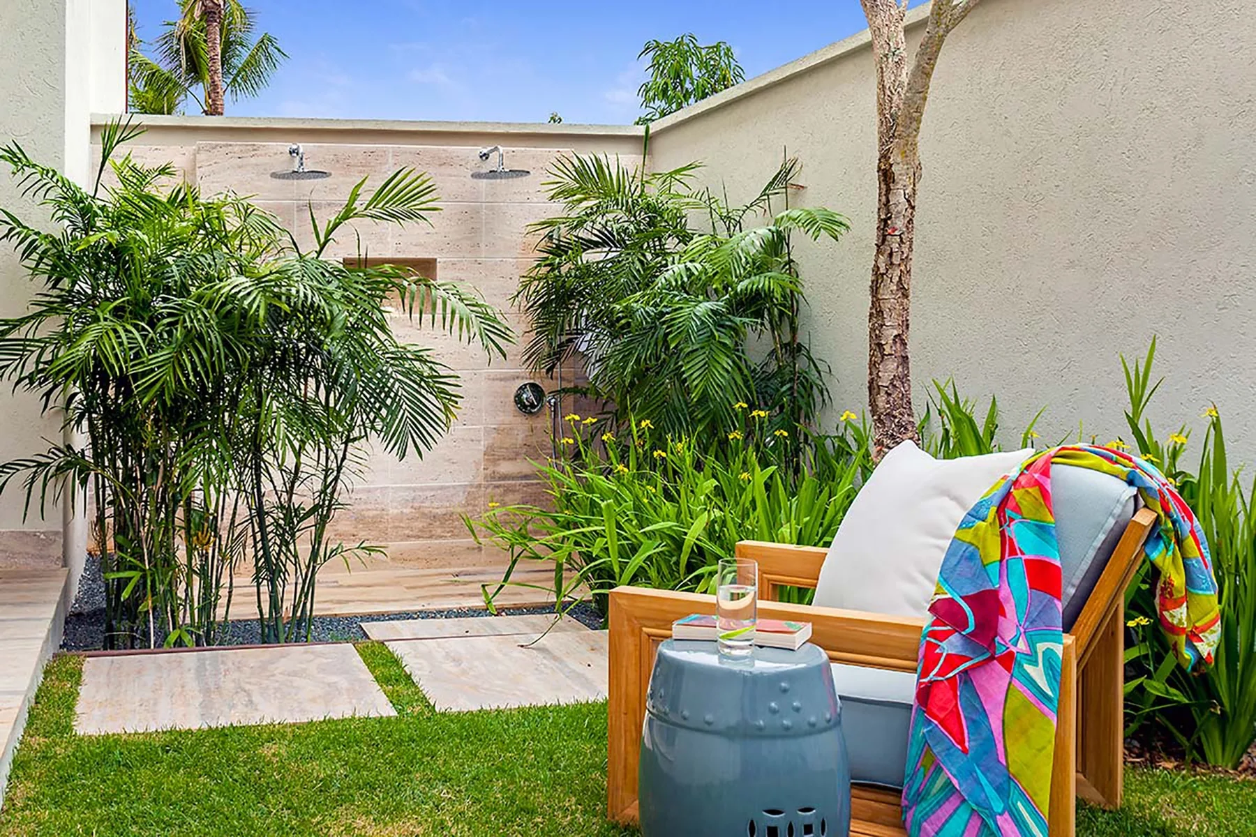 Un patio al aire libre con plantas frondosas, asientos y una ducha exterior.