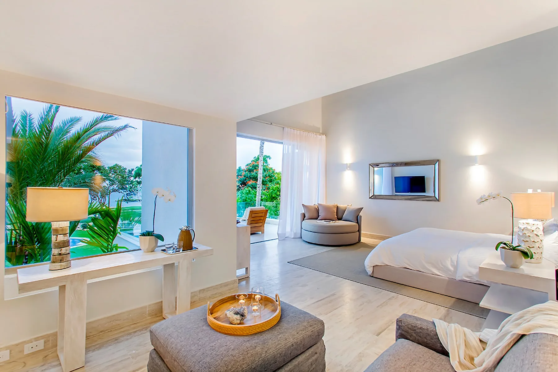 Un dormitorio luminoso con cama, zona de estar y grandes ventanas con vistas a la vegetación.