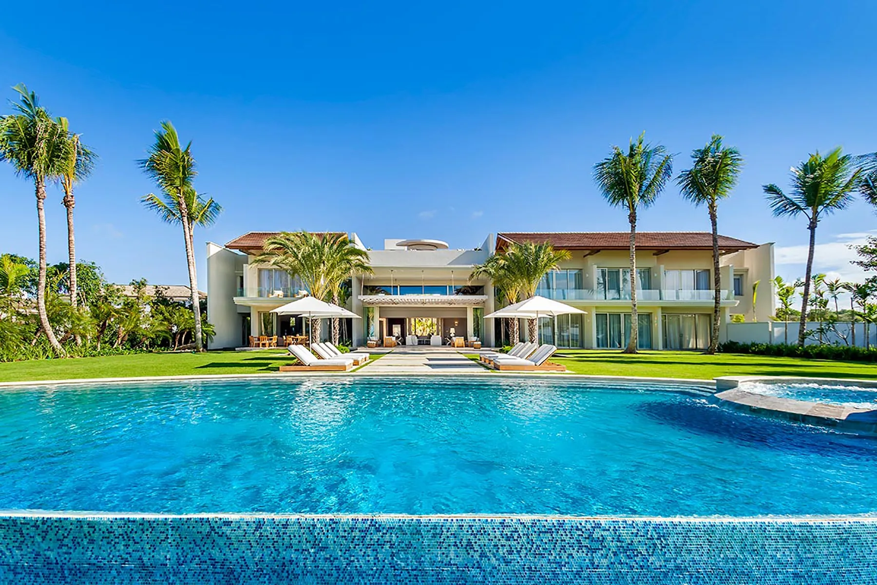 Un edificio moderno de resort da a una gran piscina rodeada de palmeras.