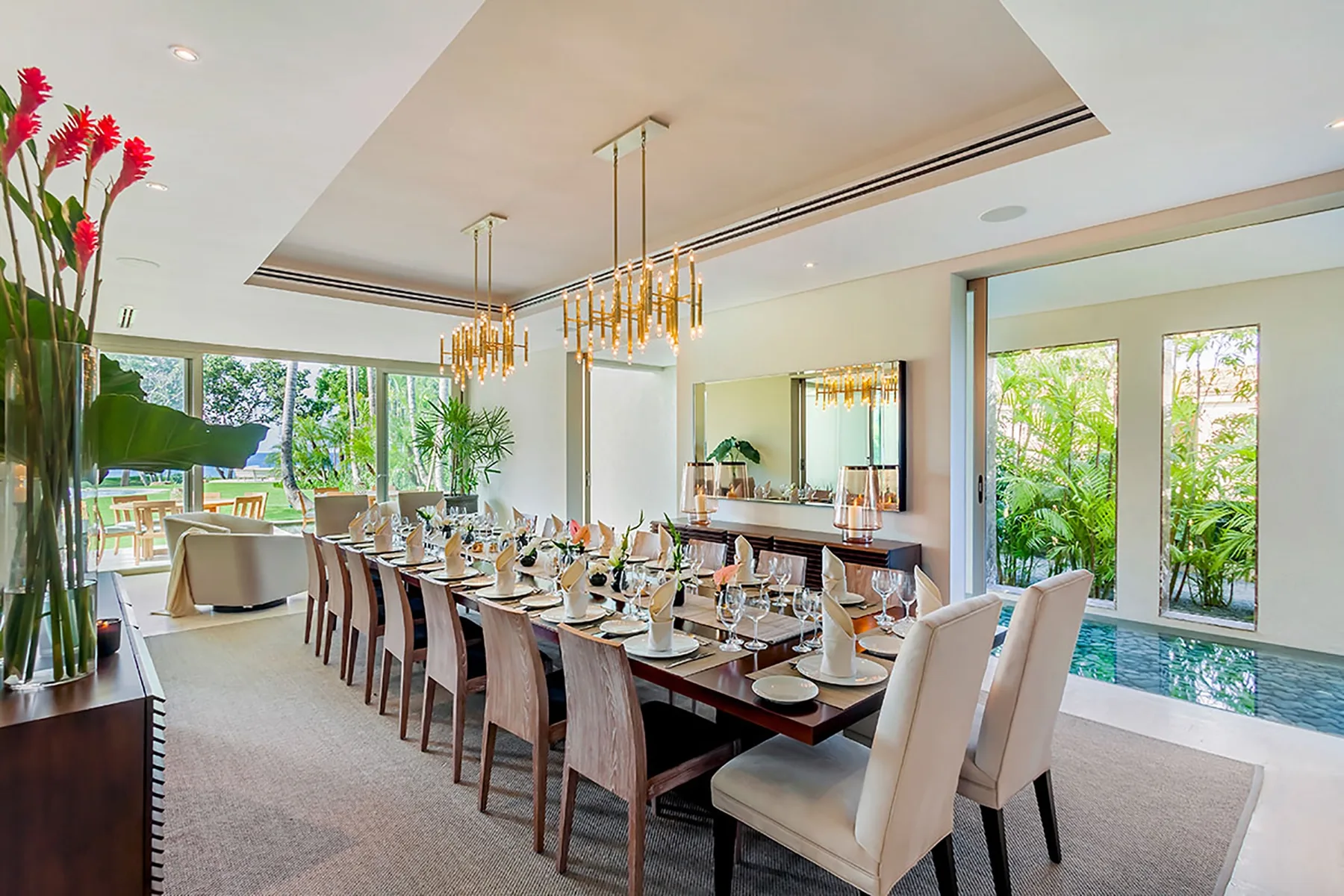 Un comedor con una mesa larga puesta con platos junto a grandes ventanas.