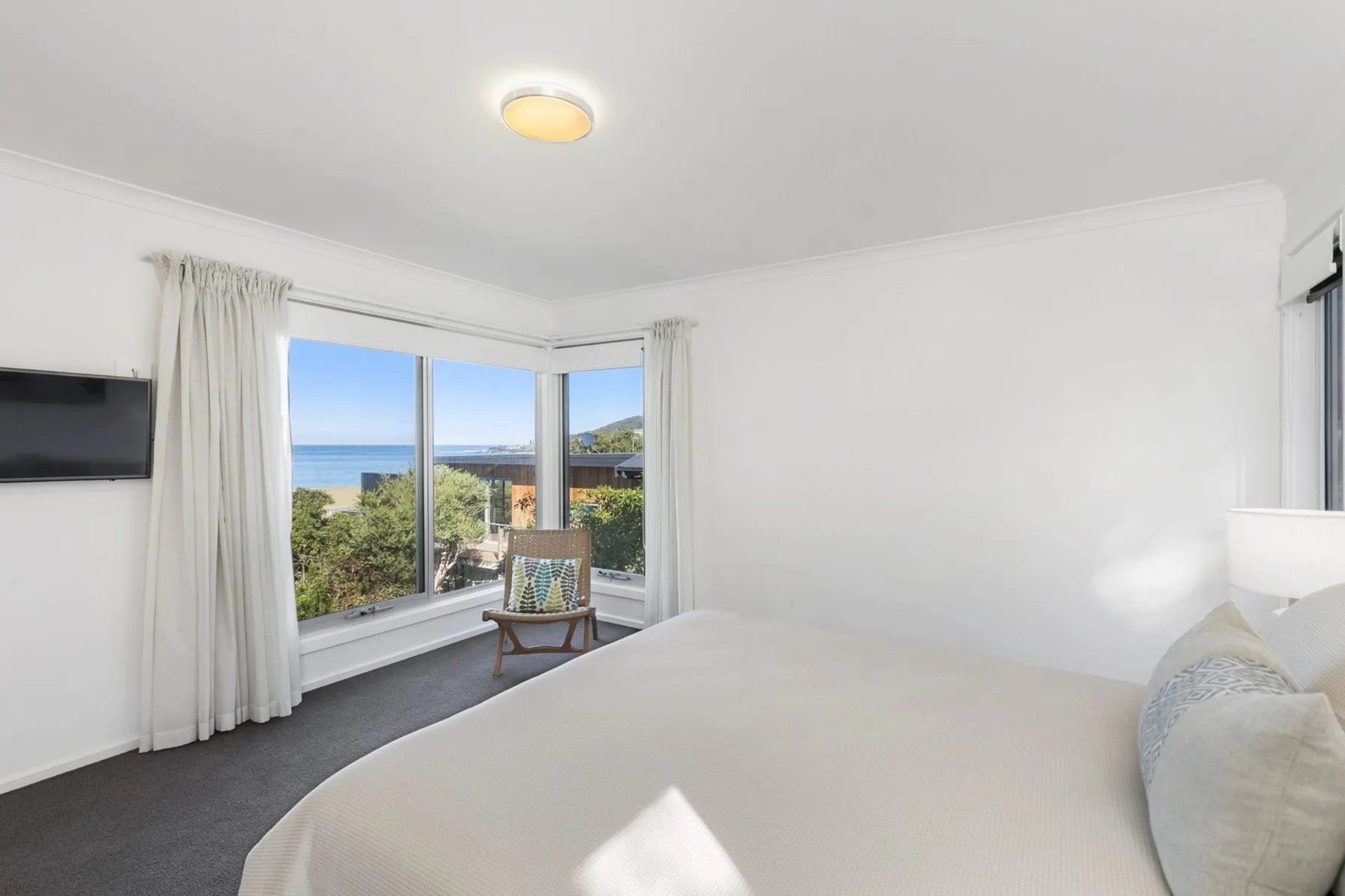 A bedroom with a bed beside corner windows overlooking the sea.