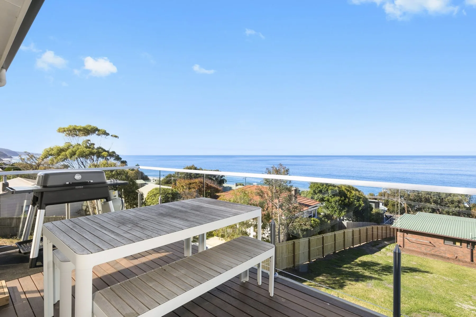 A deck with outdoor seating overlooks the ocean and a green lawn.