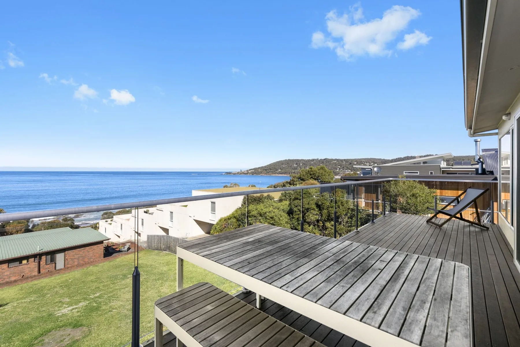 A wooden deck overlooks the ocean and nearby coastal buildings.
