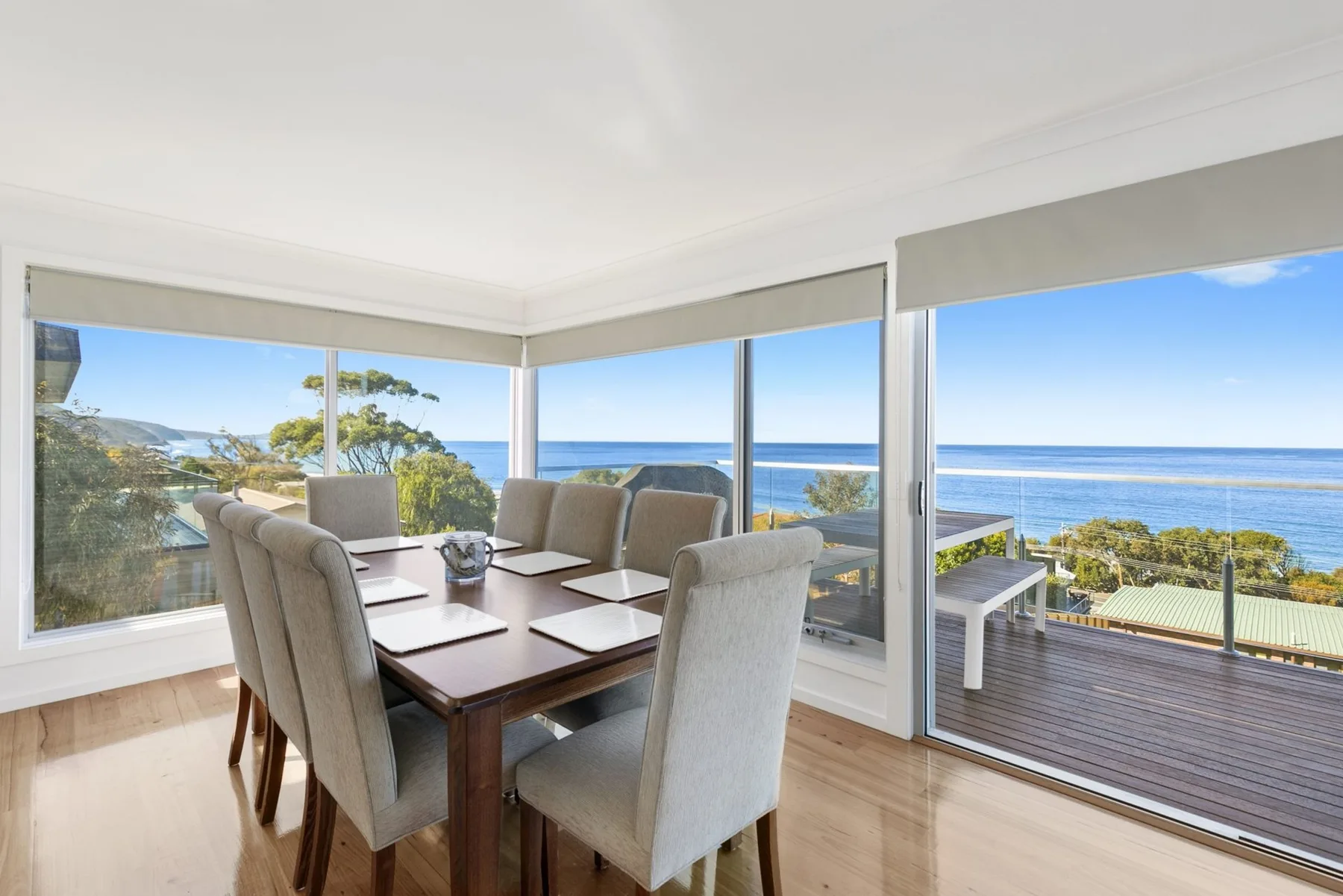 A dining area with a table and seating beside wide windows overlooking the ocean.