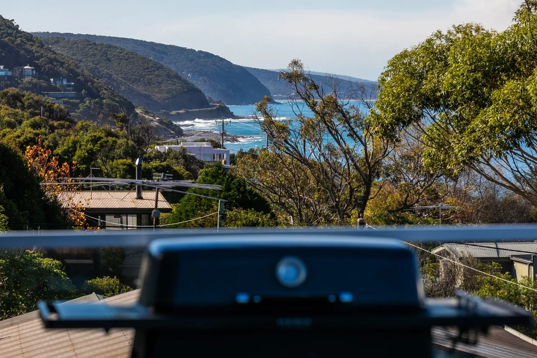 A barbecue grill overlooks a coastal bay framed by trees and hills.