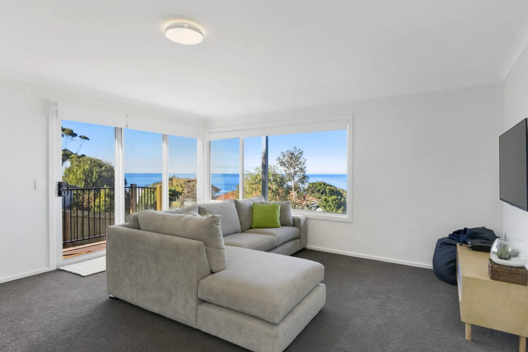 A bright living room with gray seating and large windows overlooking the sea.