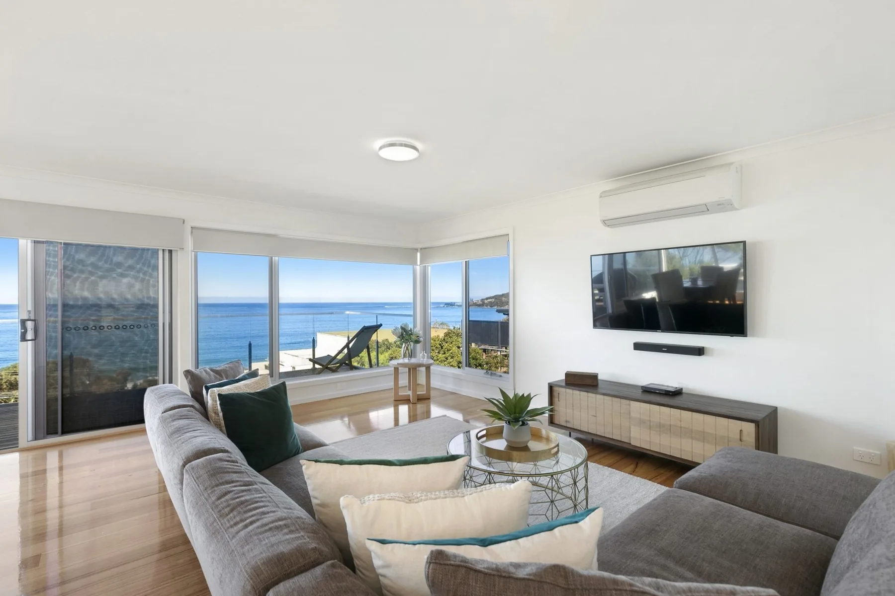 Bright living room with seating, a television, and ocean views through large windows.