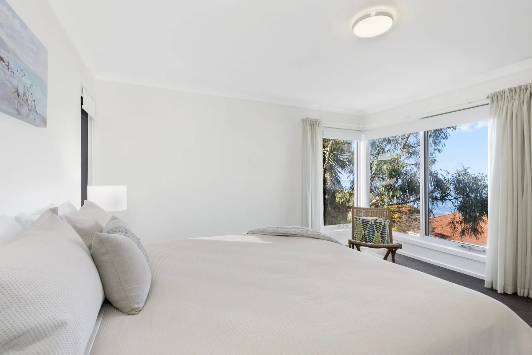 A bright bedroom with a large bed beside wide windows overlooking trees.
