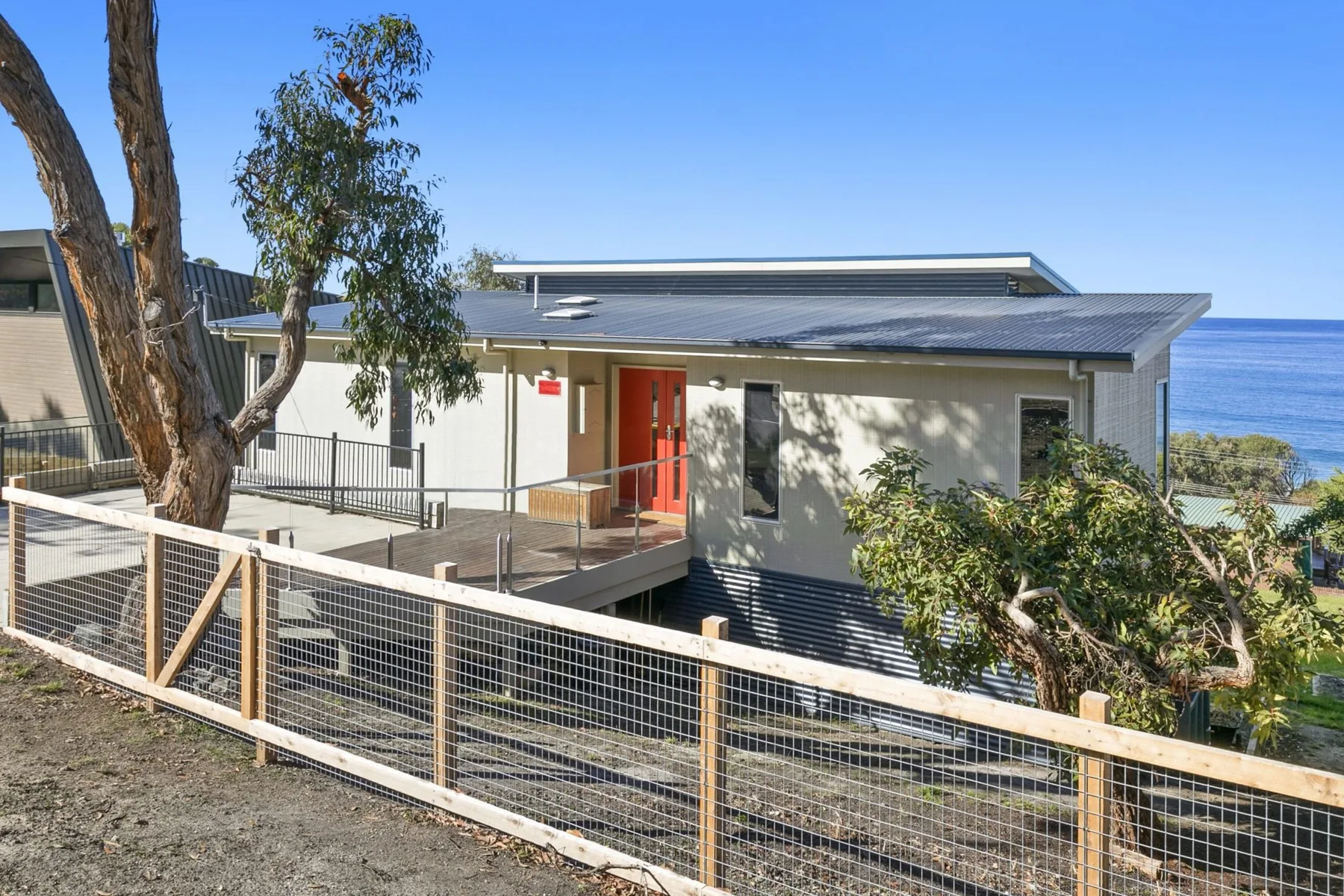 A modern coastal building with a red entrance and fenced walkway.