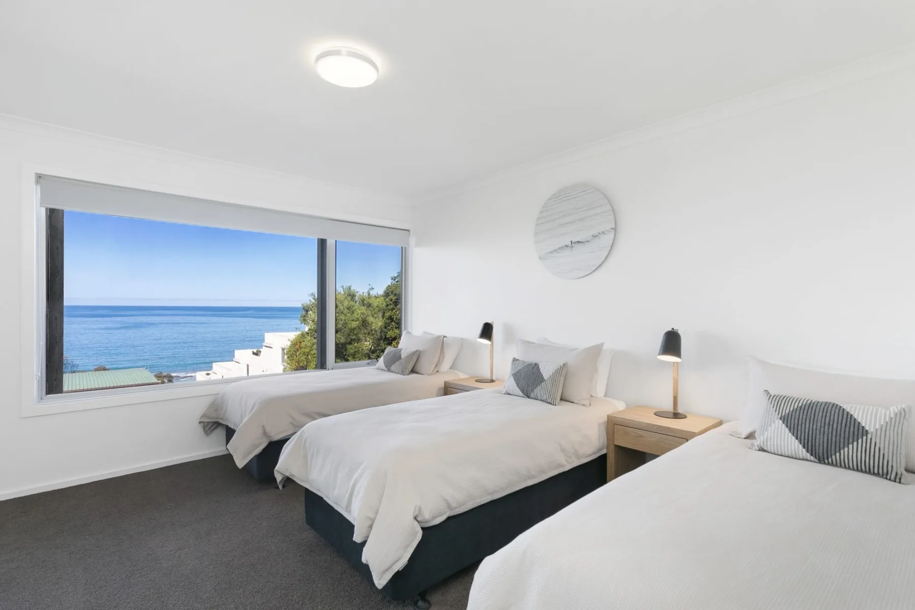 A bright bedroom with several beds beside a large window overlooking the ocean.