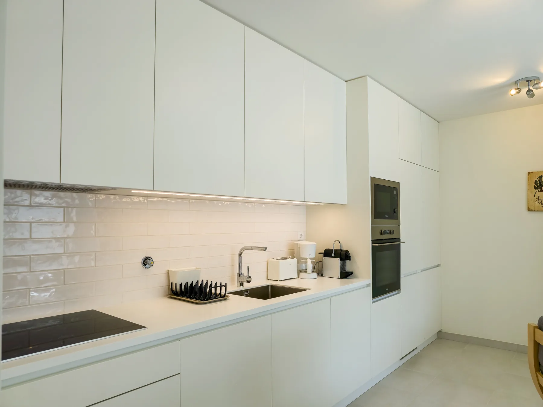 A modern kitchen with white cabinets, a cooktop, and a built-in oven.