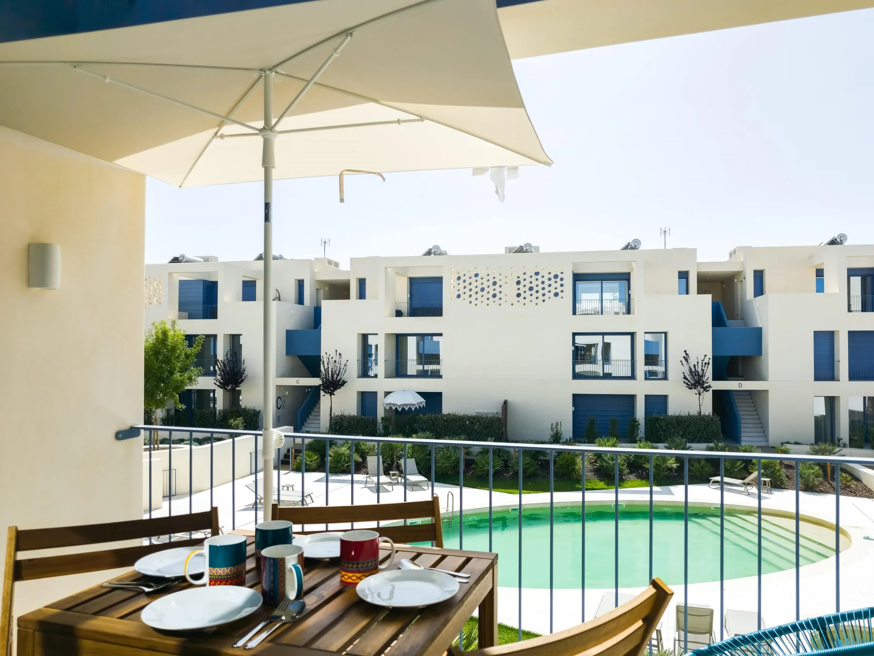 A shaded patio overlooks a swimming pool and nearby apartment buildings.