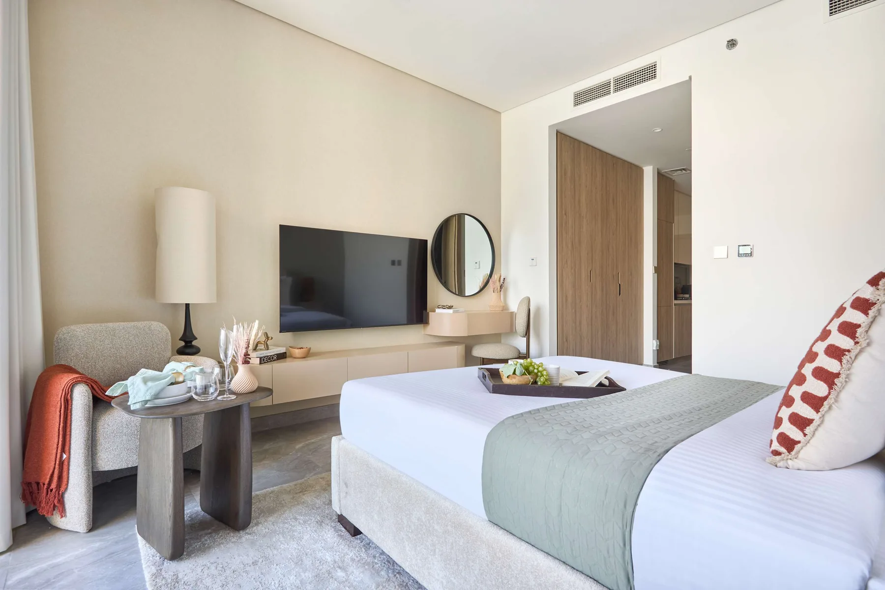 Un dormitorio luminoso con una cama bien tendida y un televisor en la pared.