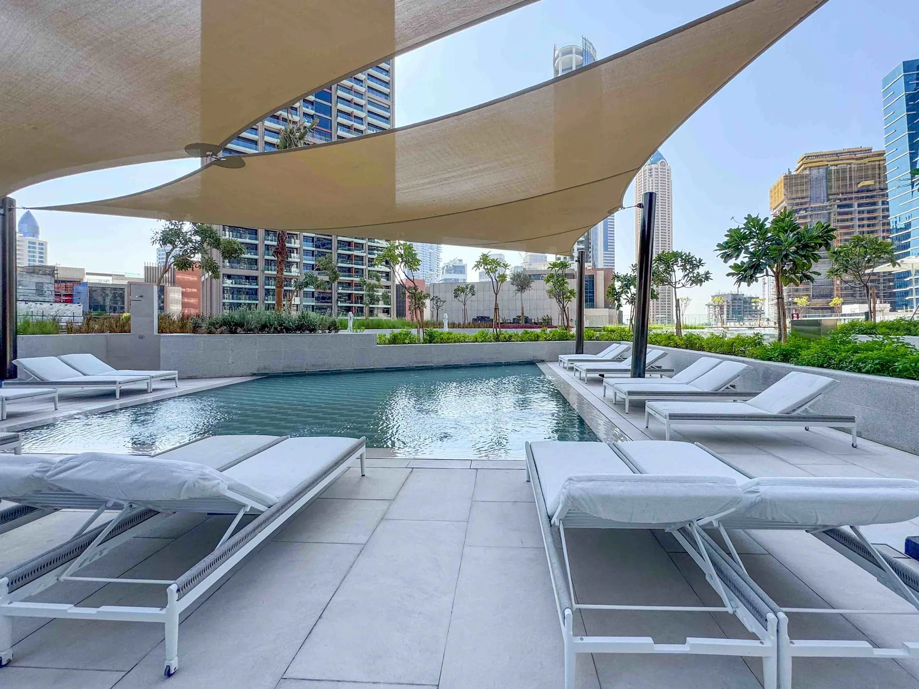 Una piscina al aire libre está rodeada de tumbonas bajo toldos de sombra.