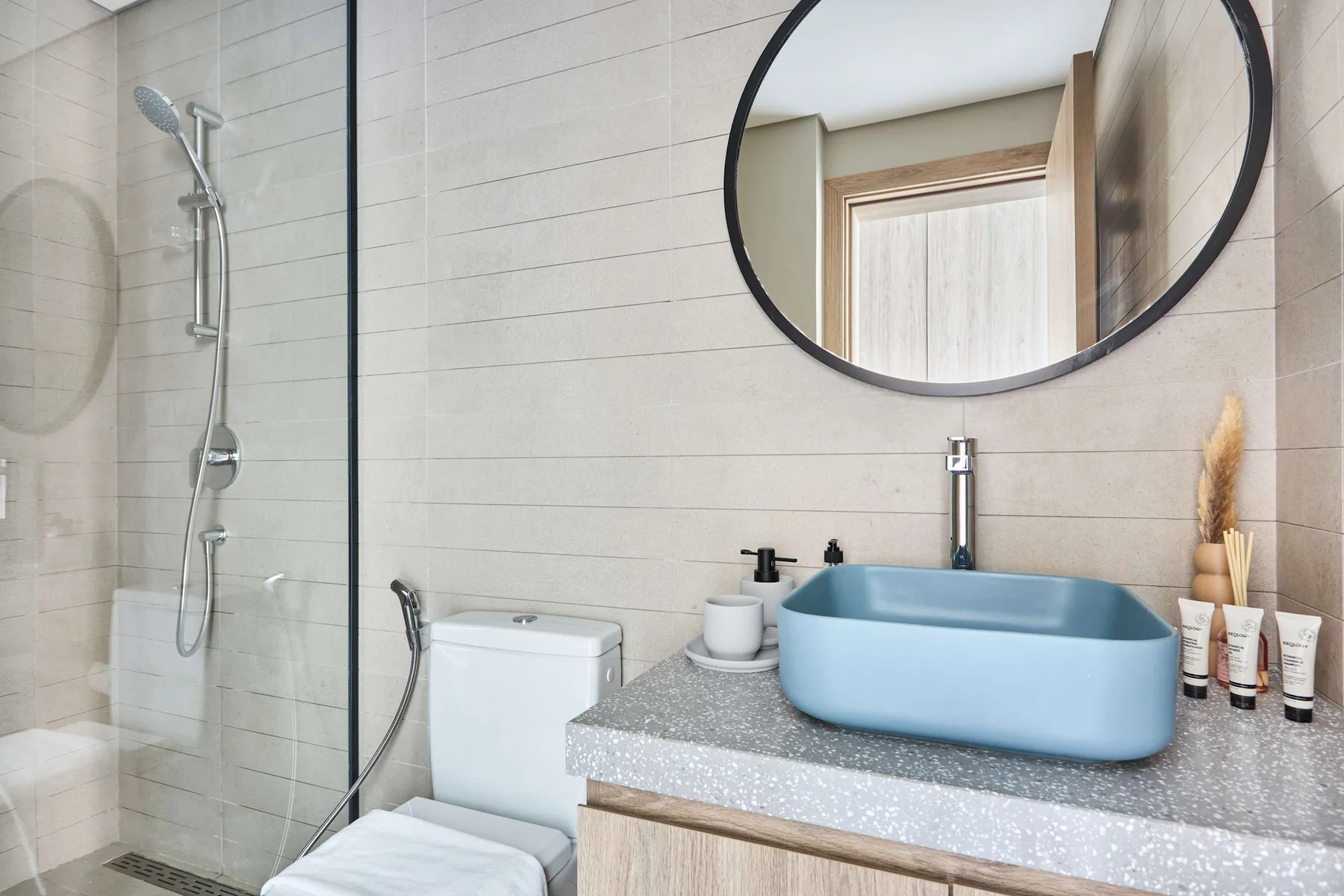 Un baño luminoso con un lavabo azul sobre encimera y una ducha de vidrio.