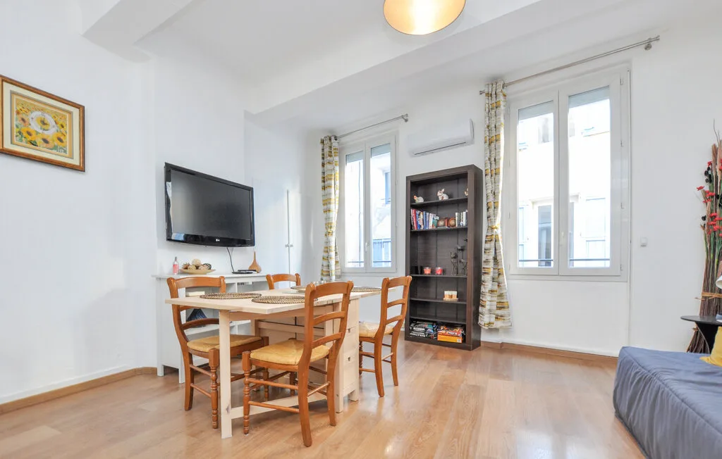 Una luminosa sala de estar y comedor con mesa, televisor y ventanas altas.