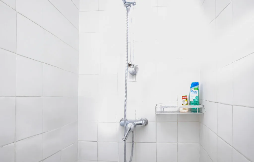 Una ducha con azulejos, una ducha de mano y artículos de aseo en un estante.