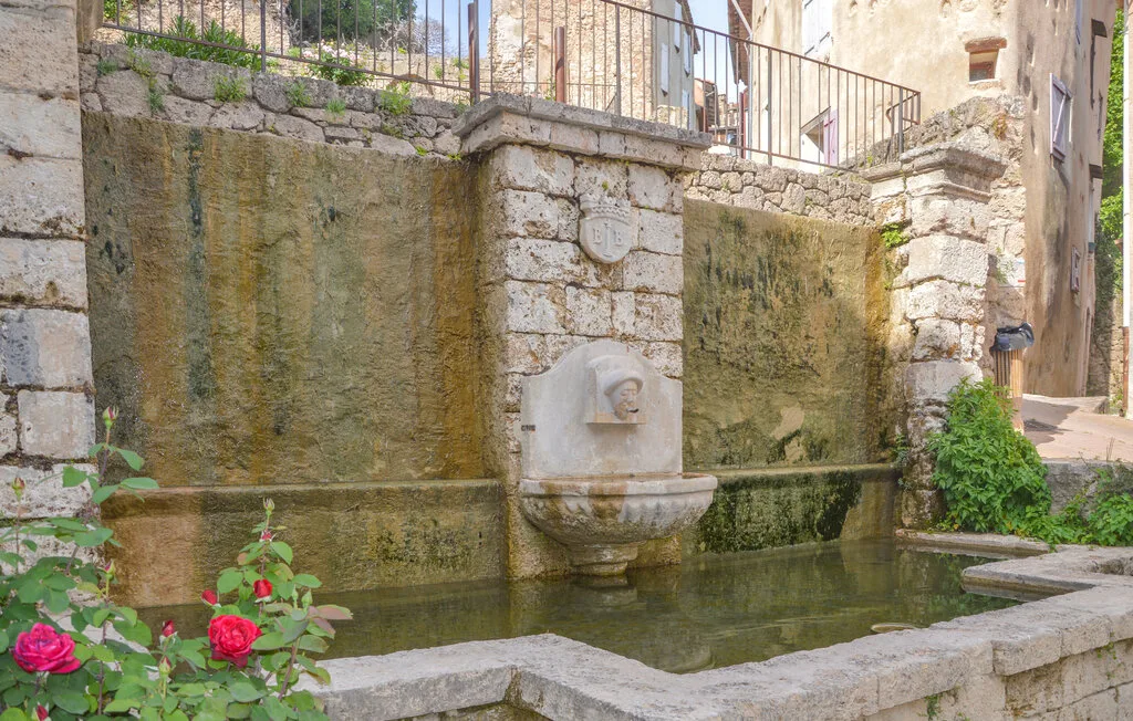 Una fuente de piedra está en una pila poco profunda junto a un muro de mampostería.