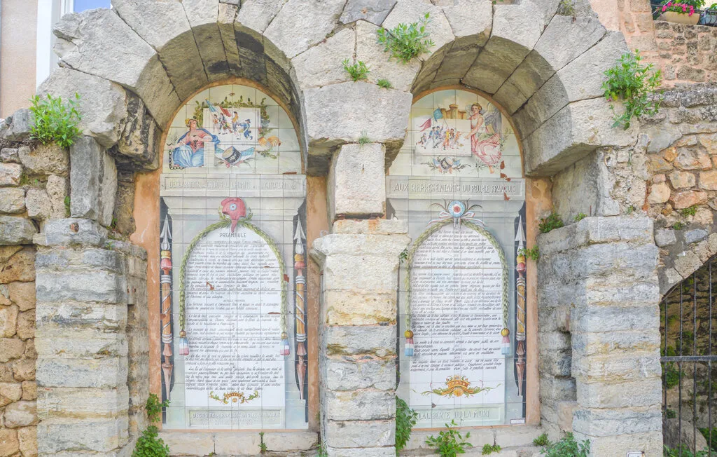 Dos nichos de piedra decorados, con paneles pintados e inscripciones, están en un muro exterior.