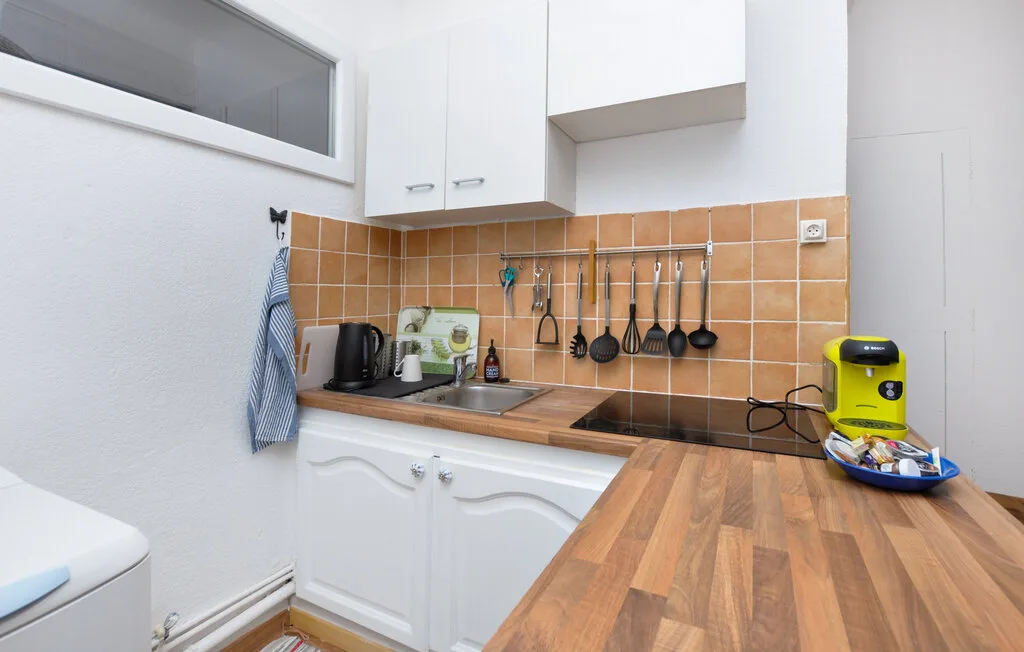 Una cocina compacta con armarios blancos, salpicadero de azulejos y encimera de madera.