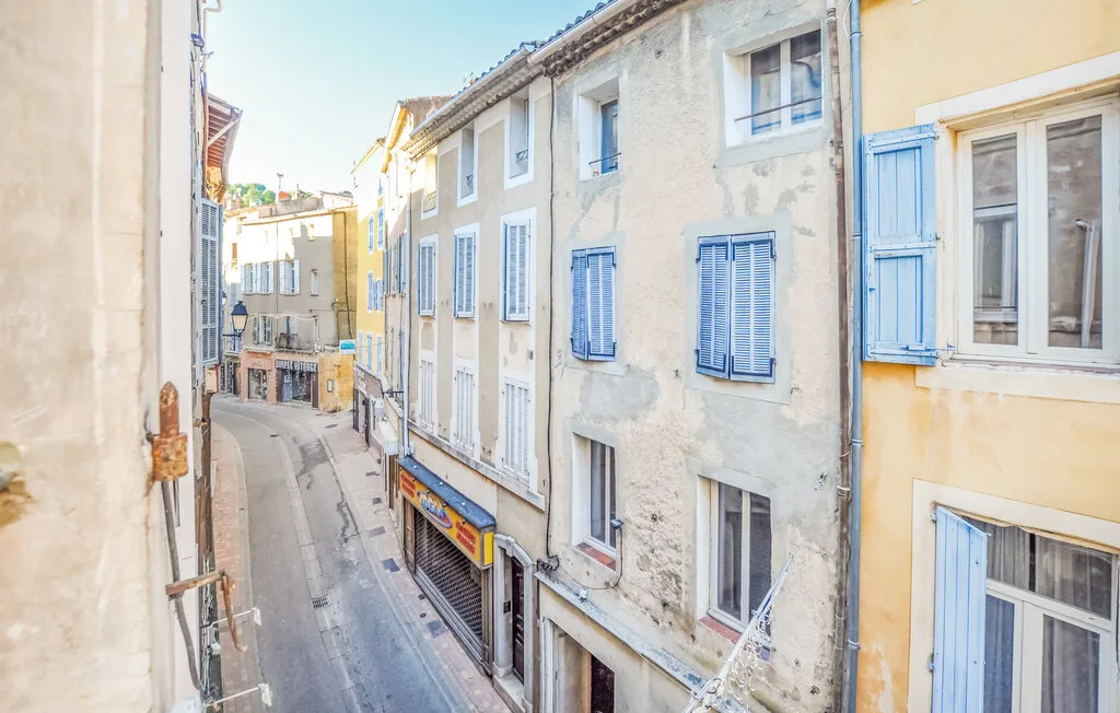 Una calle estrecha pasa entre hileras de edificios claros con contraventanas azules.