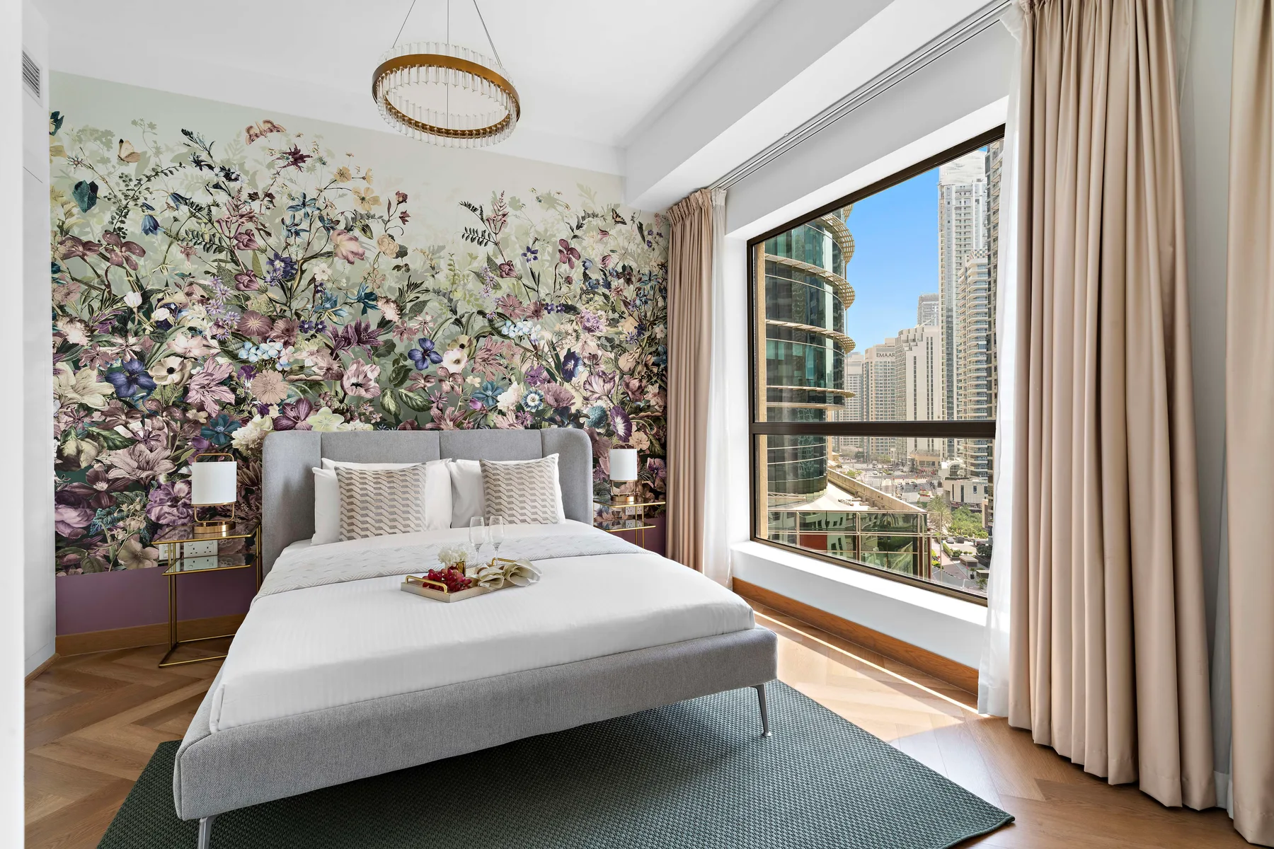 A bedroom with a bed against a floral wall and a large window.