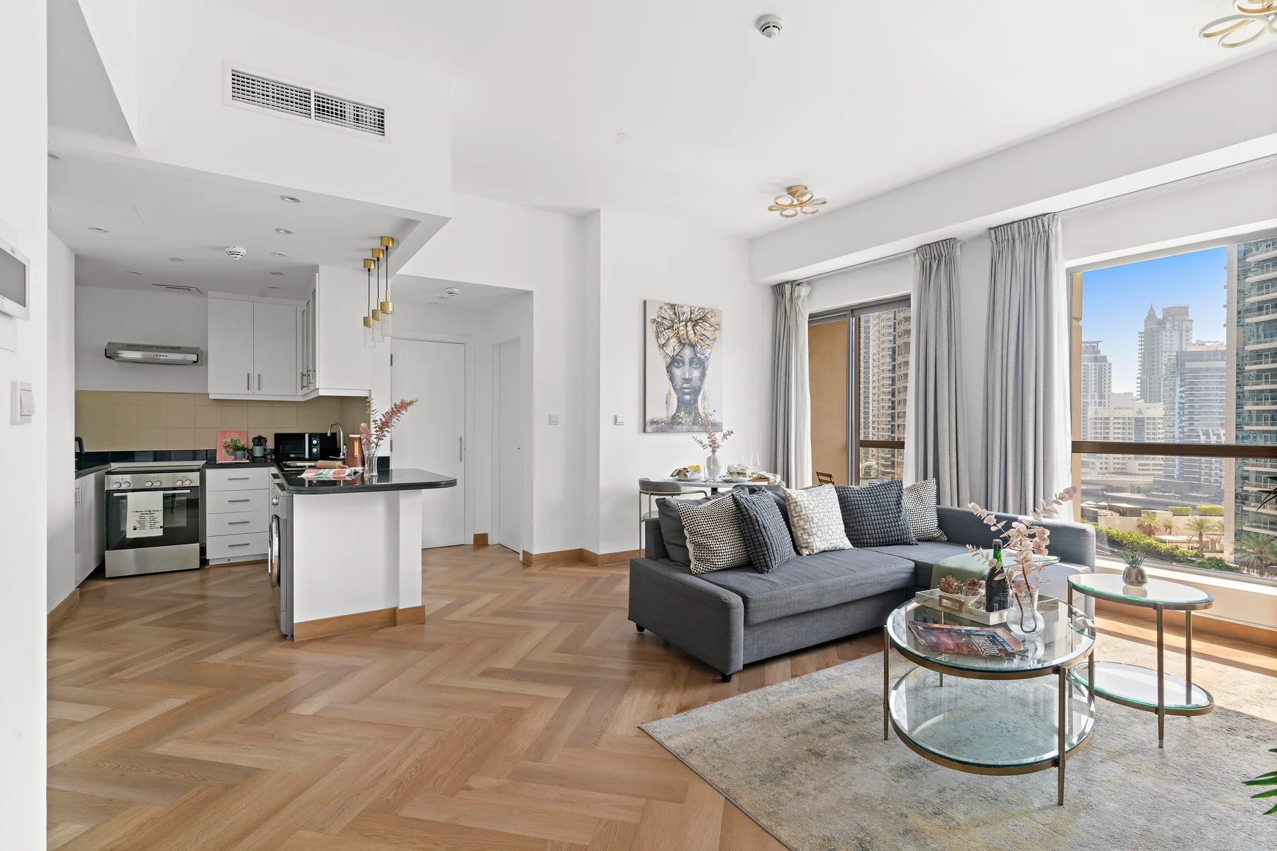 A bright open-plan living room and kitchen with seating beside large windows.