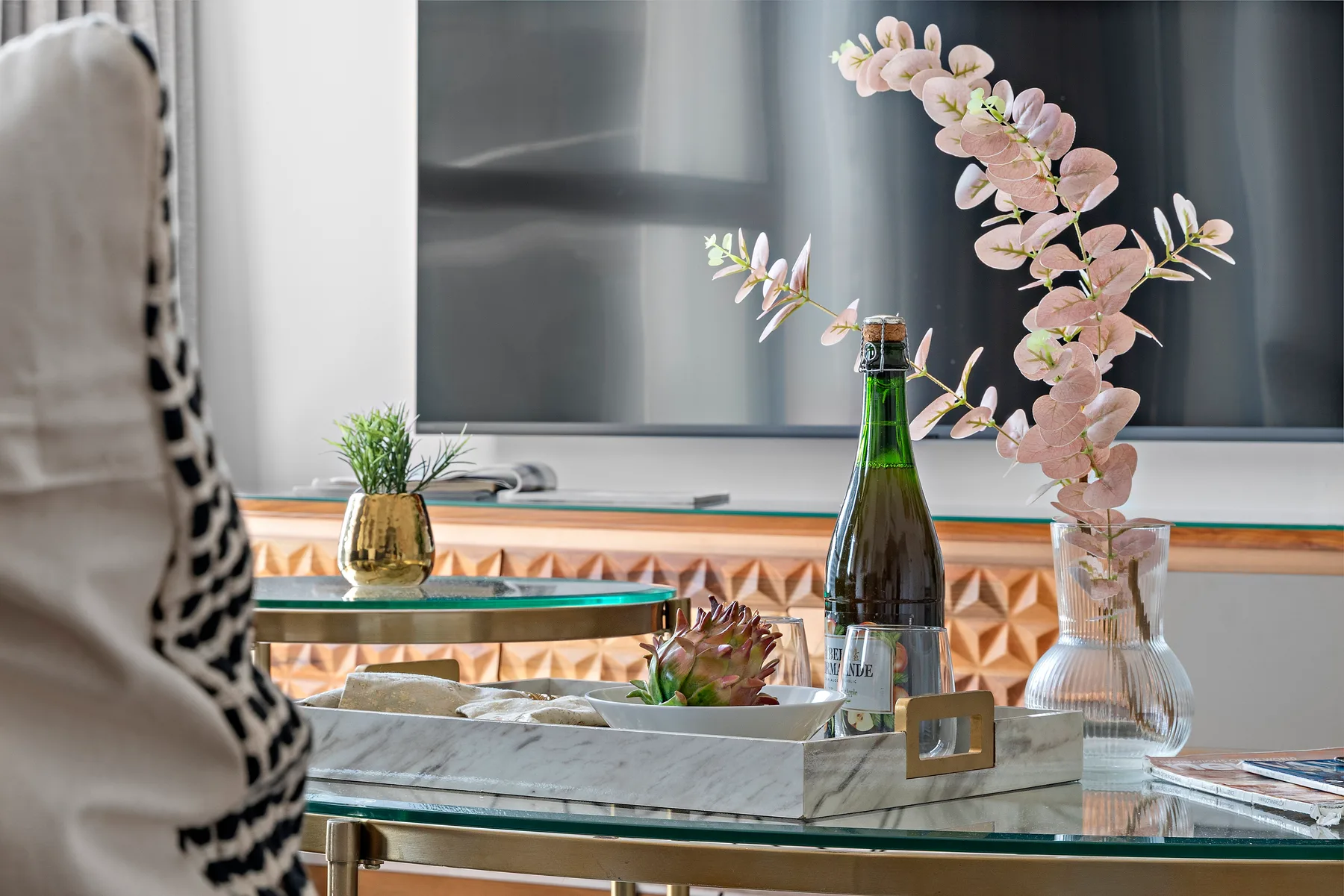 A lounge seating area features a glass table with a bottle, flowers, and a decorative tray.