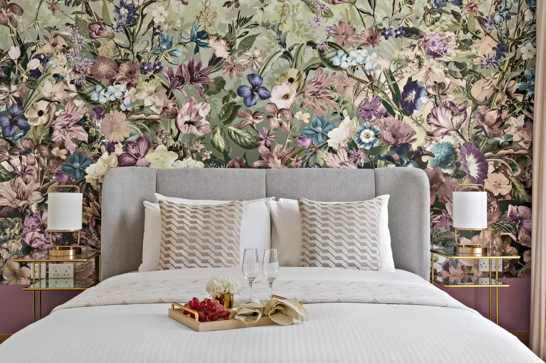 A bedroom with a bed against a colorful floral wall.