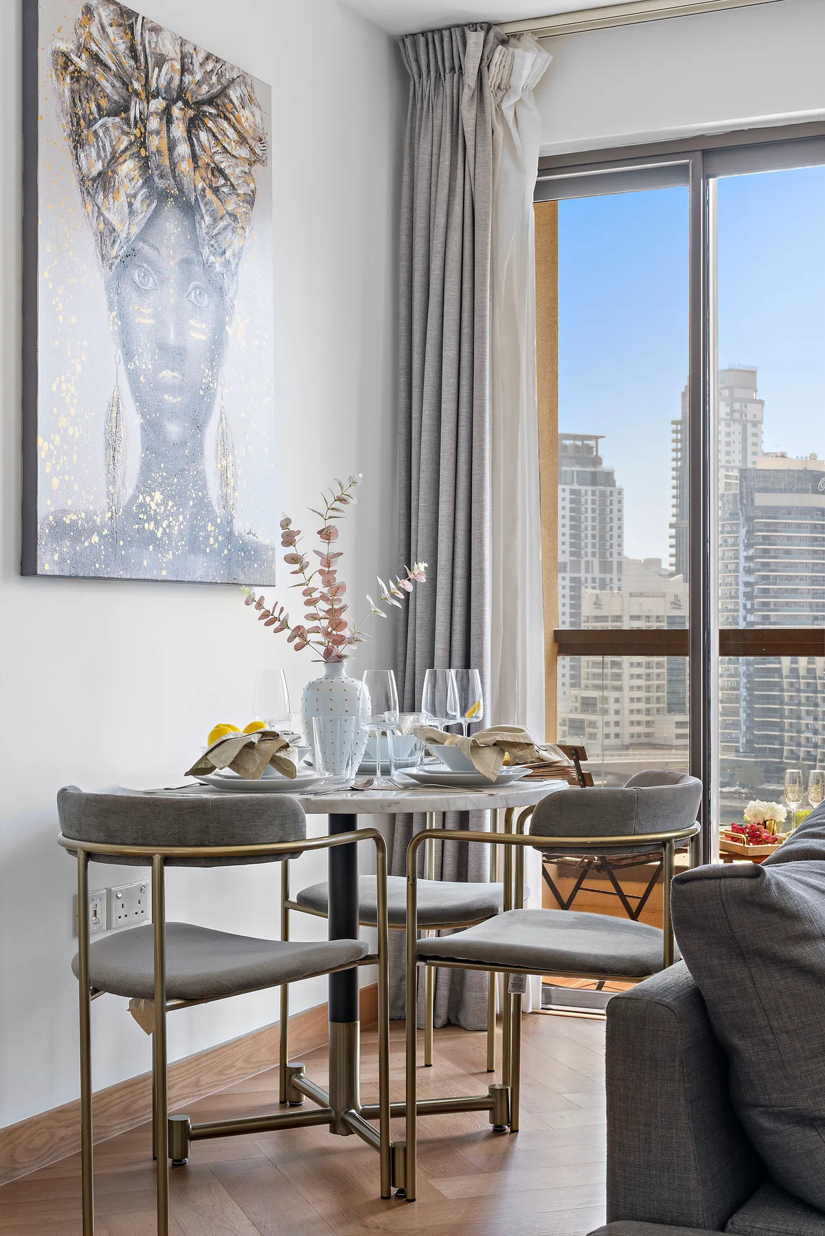 A dining area with a set table beside large windows overlooking nearby buildings.