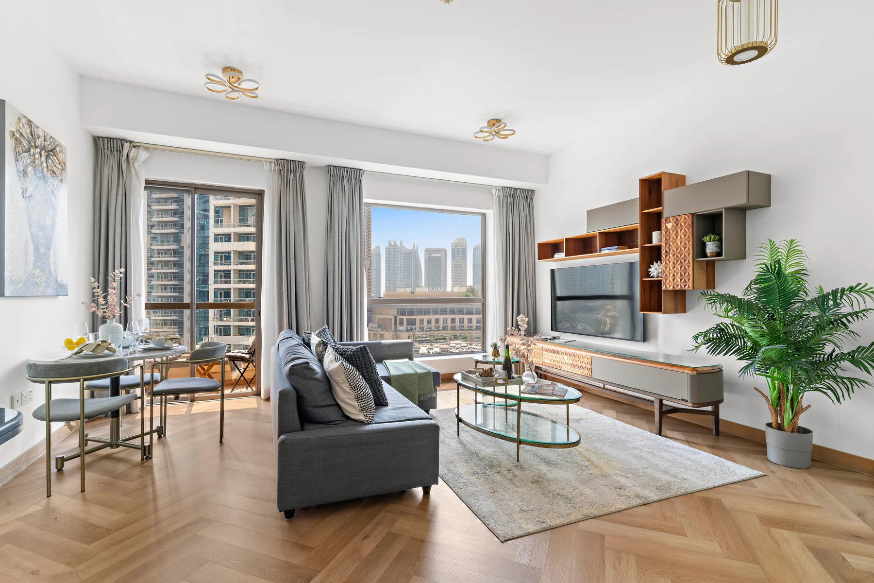 A bright living room with seating, a television, and large windows overlooking city buildings.