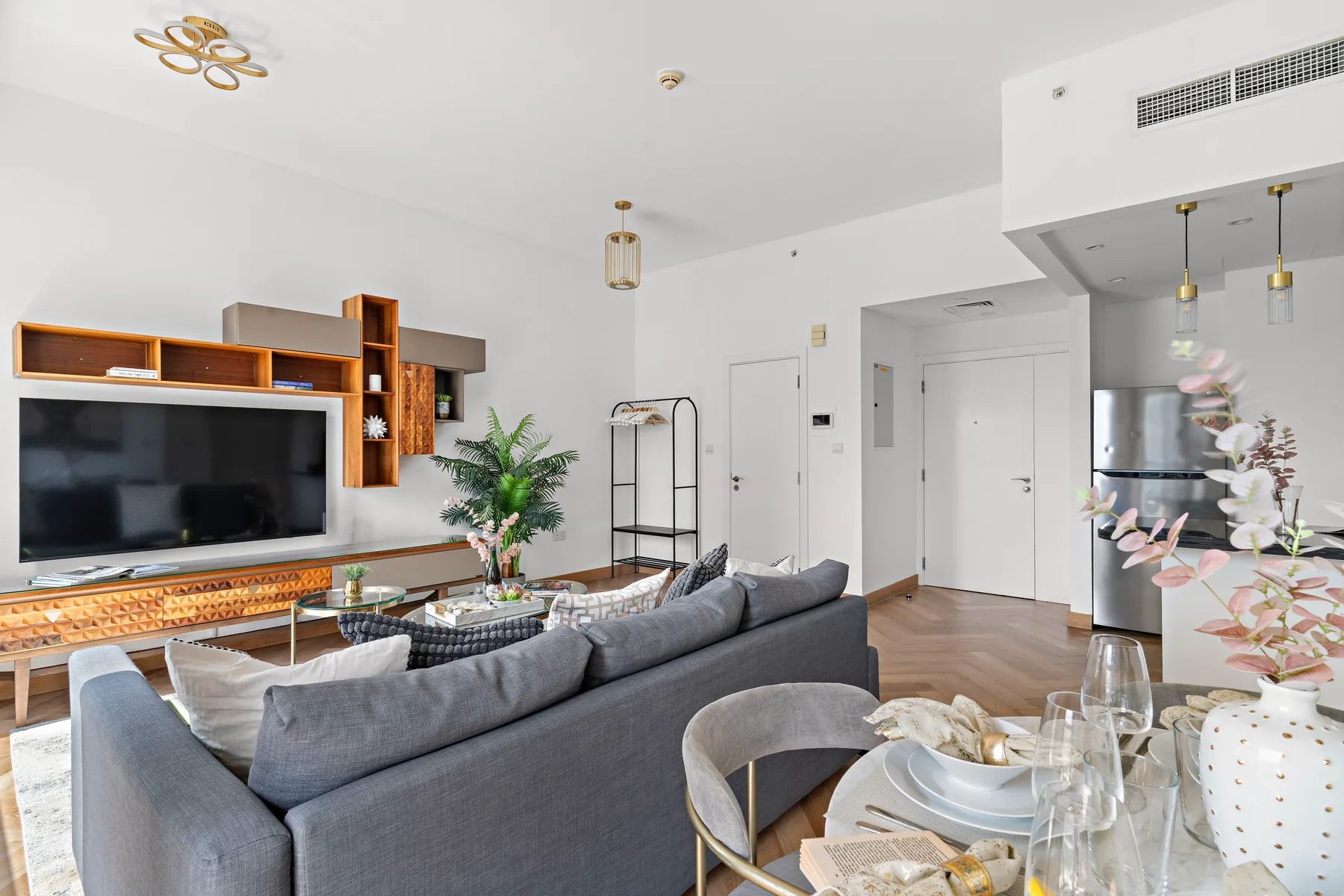 A bright living room with gray seating, a television, and a dining table.
