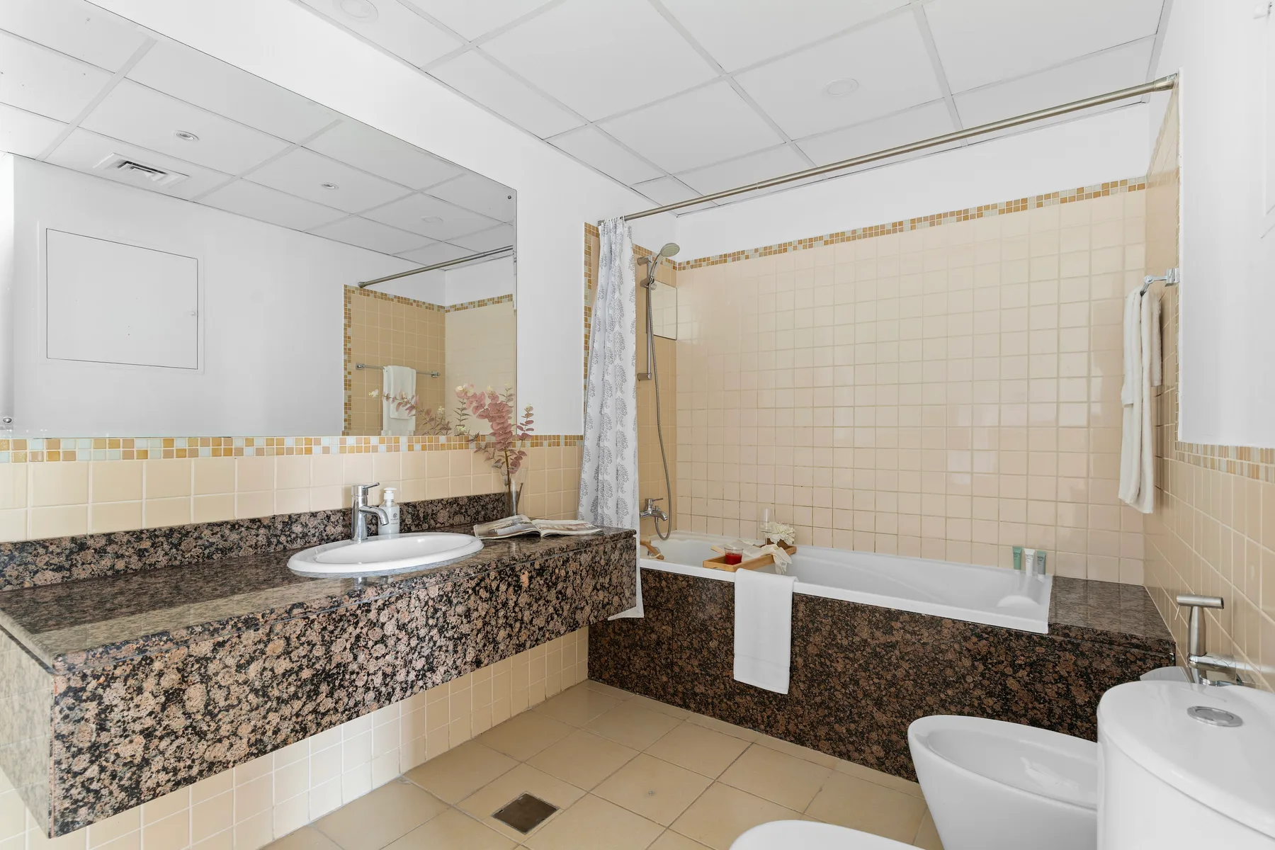 A tiled bathroom with a bathtub, sink, and large mirror.