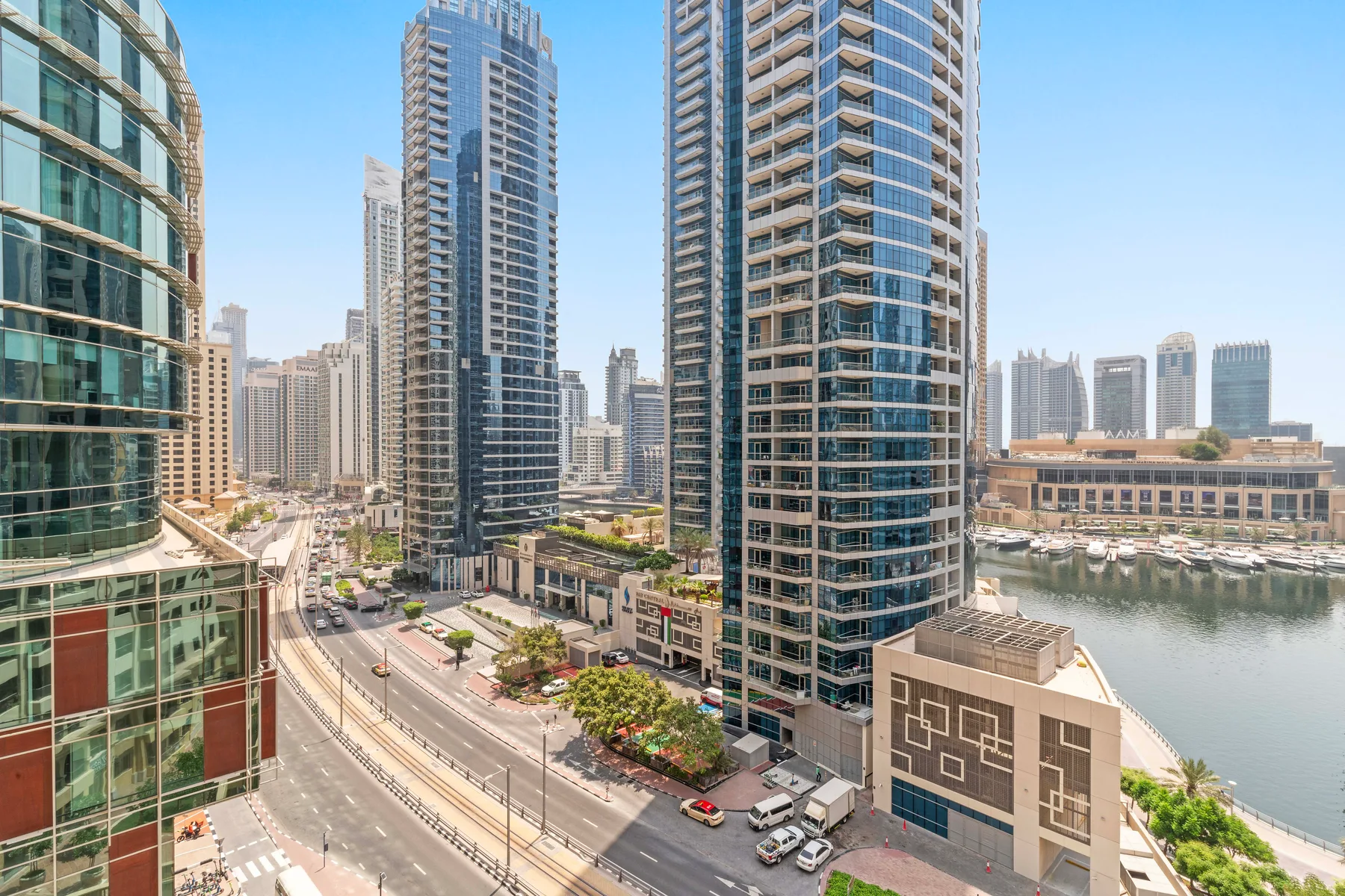 A city street runs between tall modern buildings beside a waterfront.