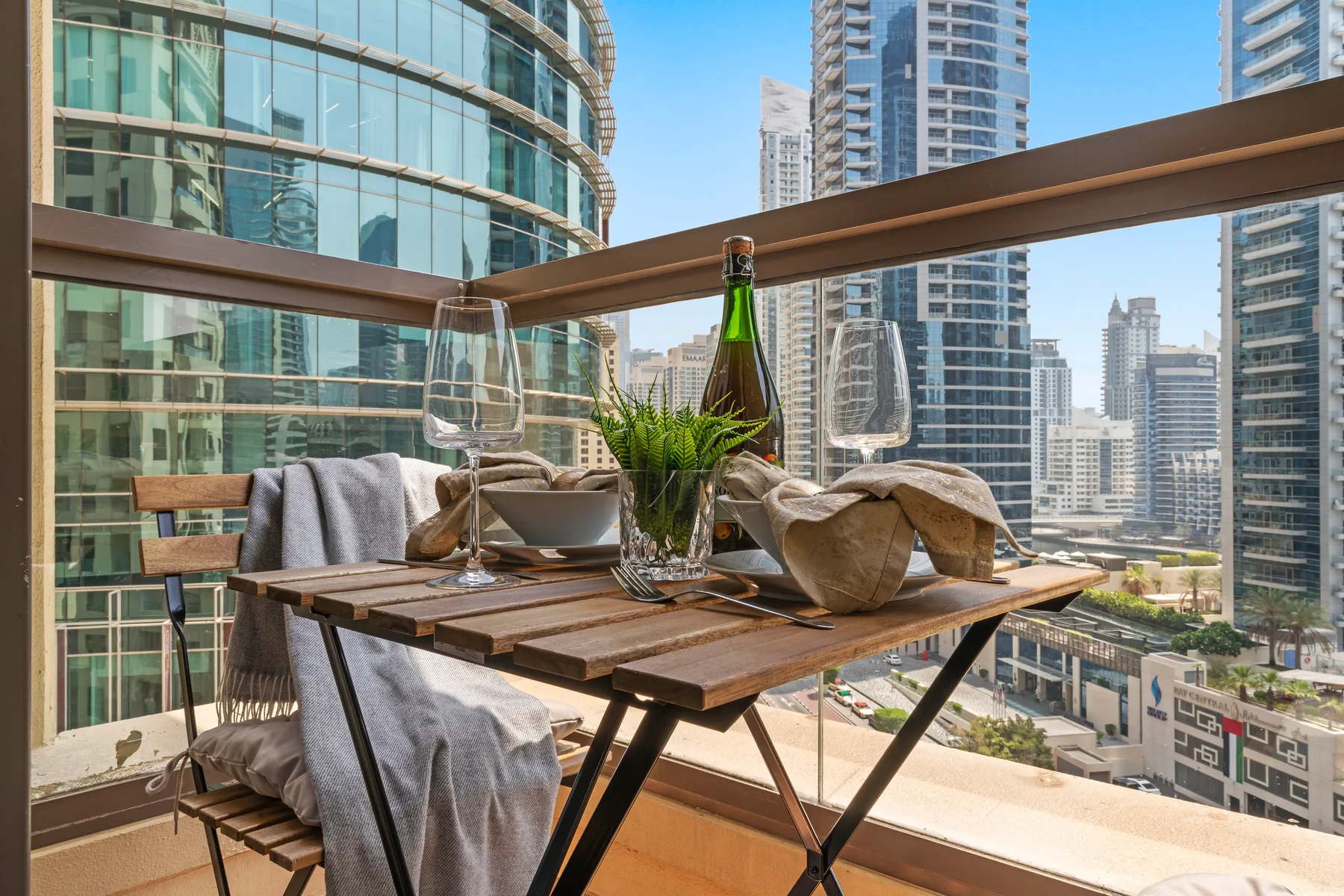 A balcony dining table with place settings overlooks a cluster of high-rise buildings.