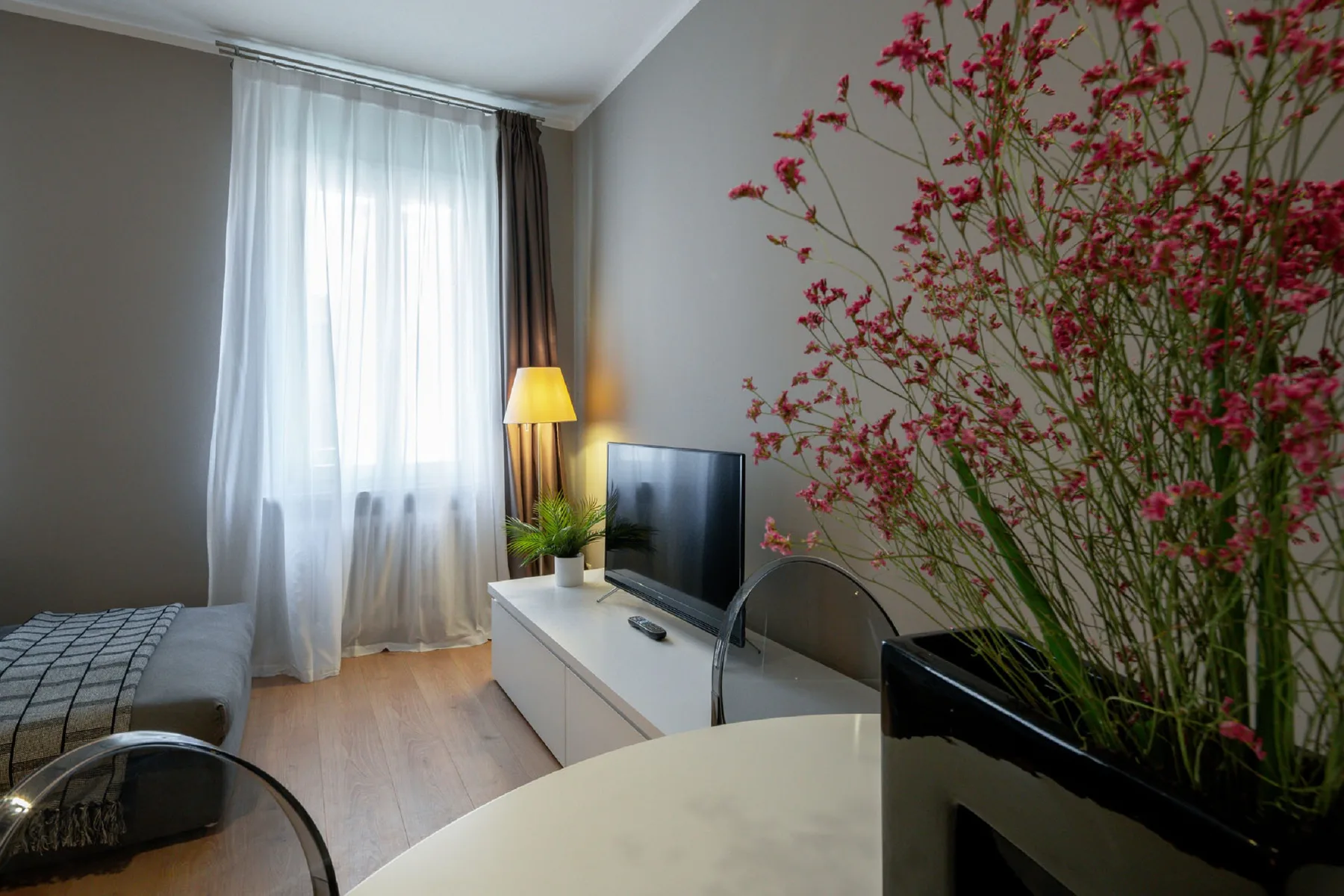 Un dormitorio con cama, televisor y ramas altas en flor junto a la ventana.