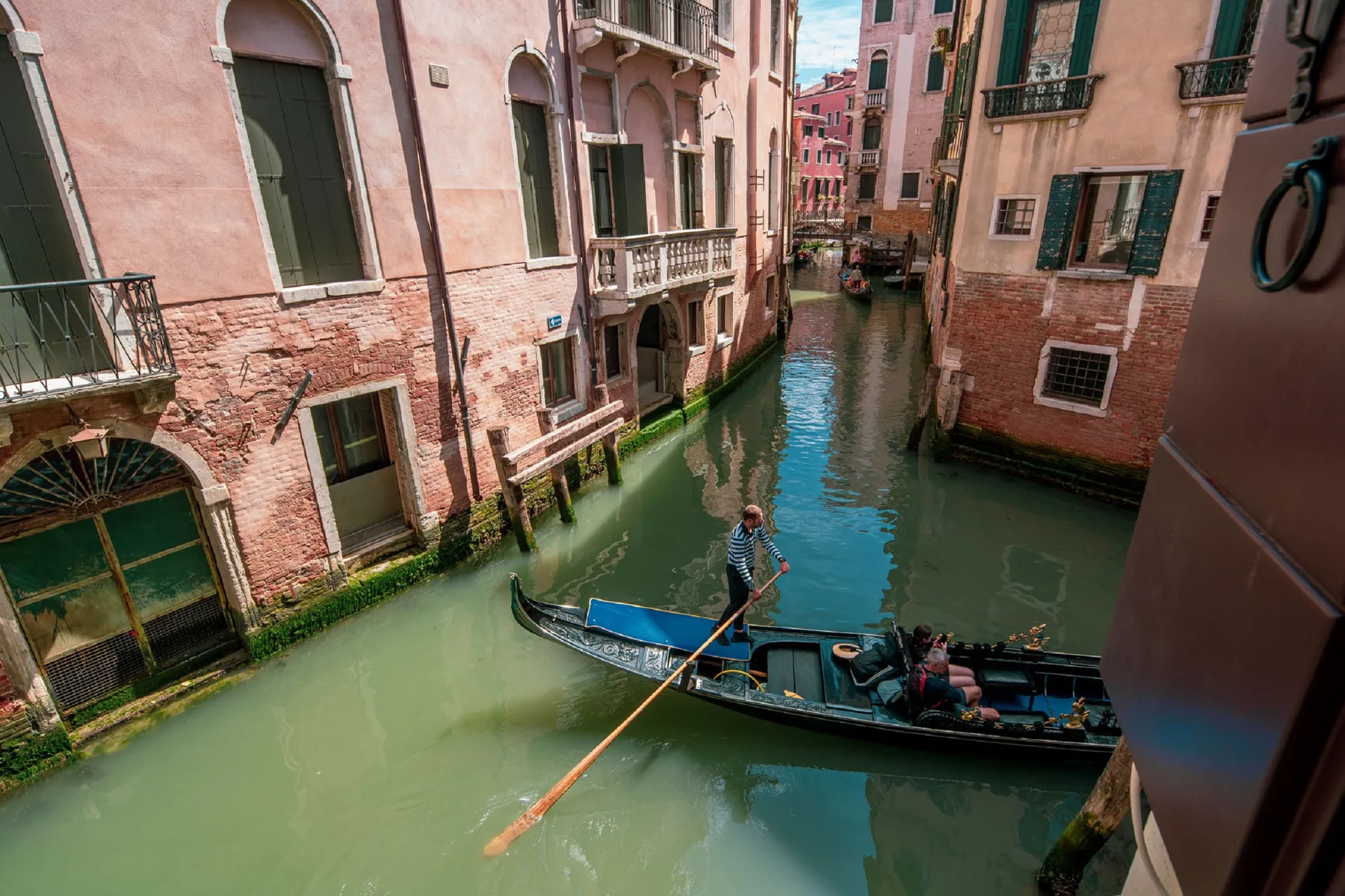 Una góndola avanza por un canal estrecho entre edificios muy próximos.