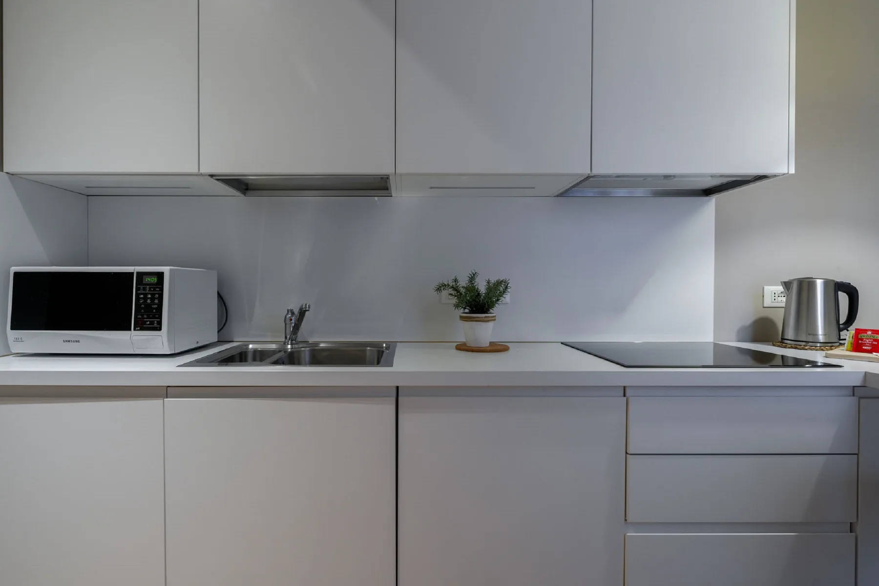 Una cocina moderna con microondas, fregadero y pequeños electrodomésticos sobre la encimera.