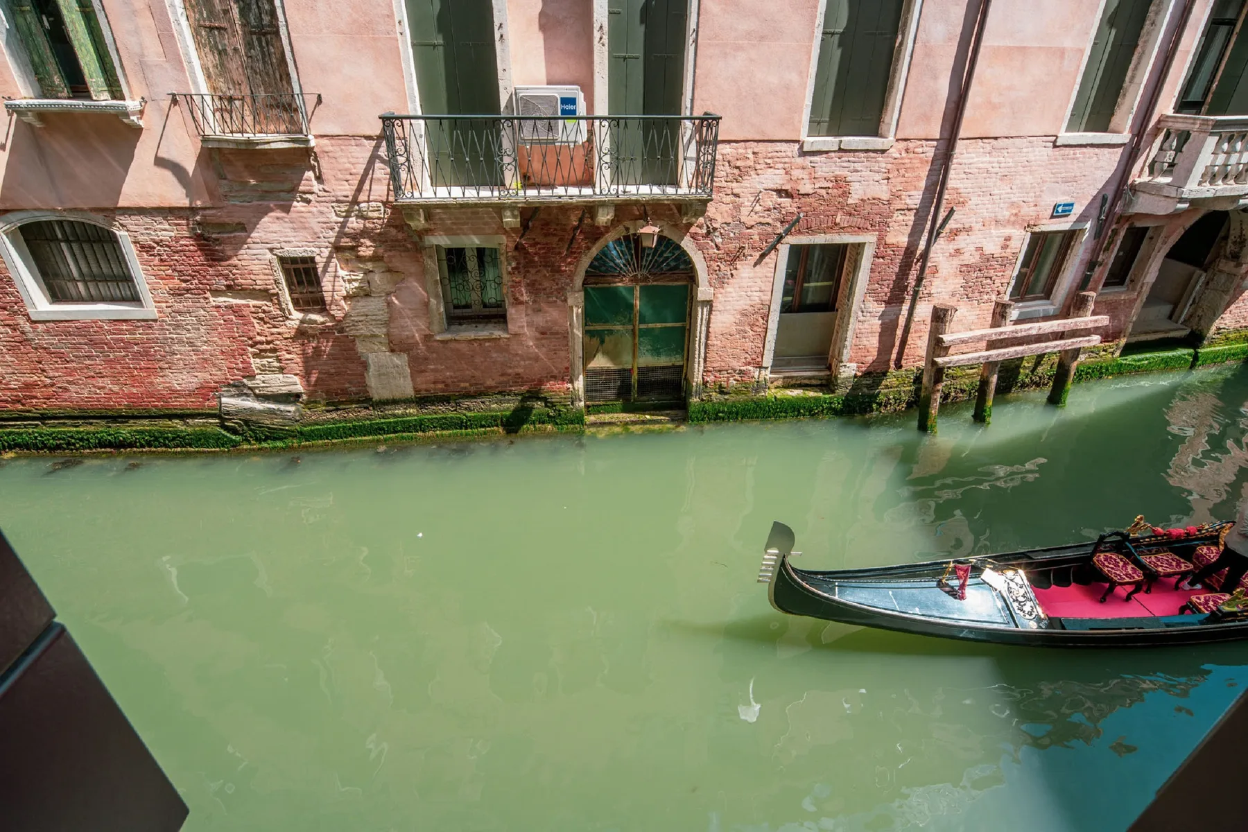 Un canal pasa junto a un edificio rosa desgastado, con una góndola en el agua.