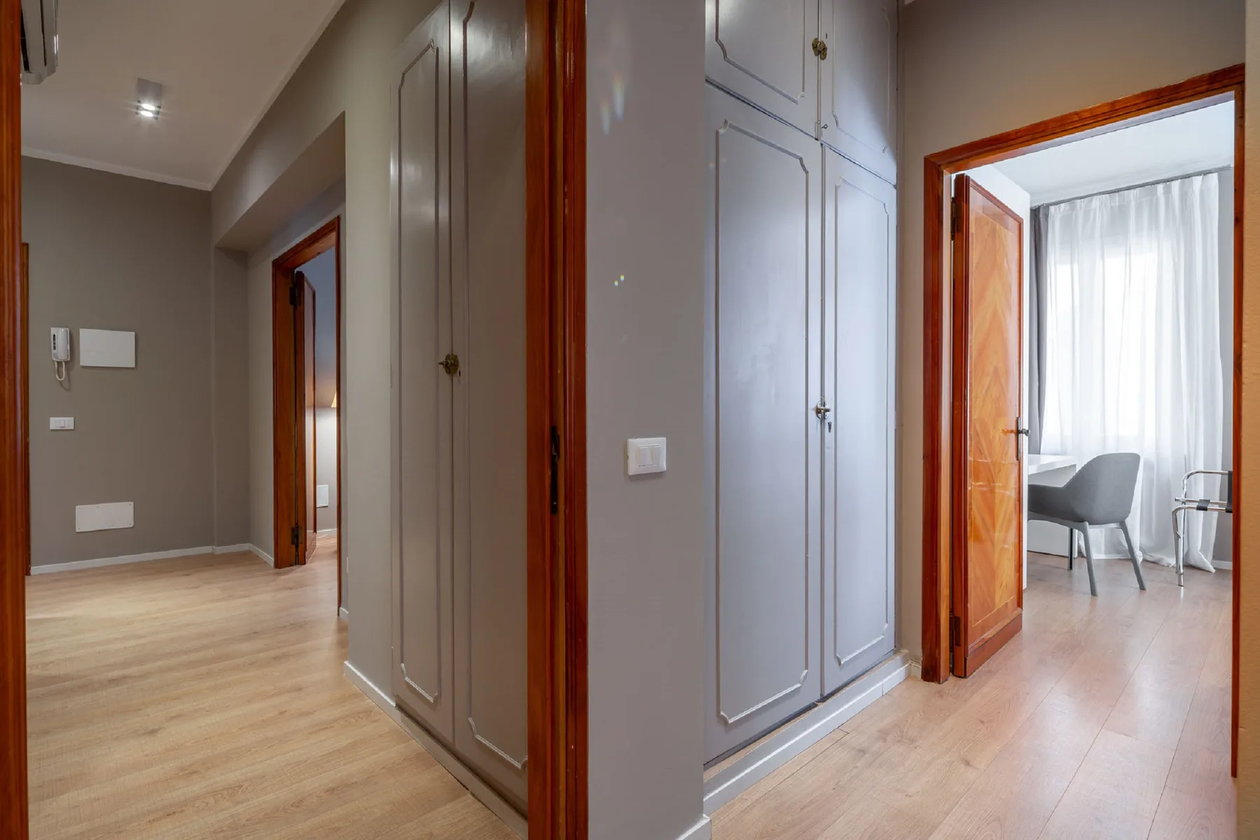 Un pasillo con armarios empotrados conduce a una habitación luminosa con asientos junto a una ventana.