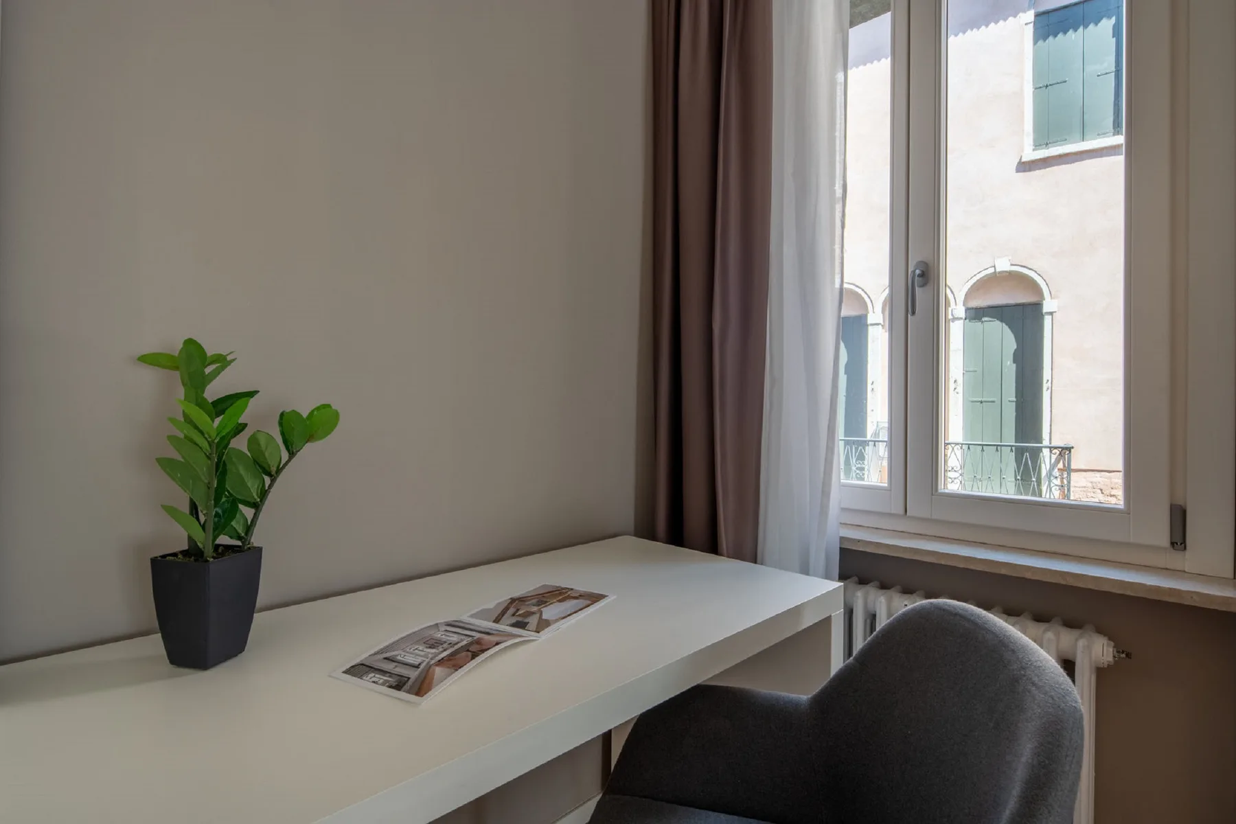 Un escritorio junto a una ventana, con una planta en maceta y una silla.