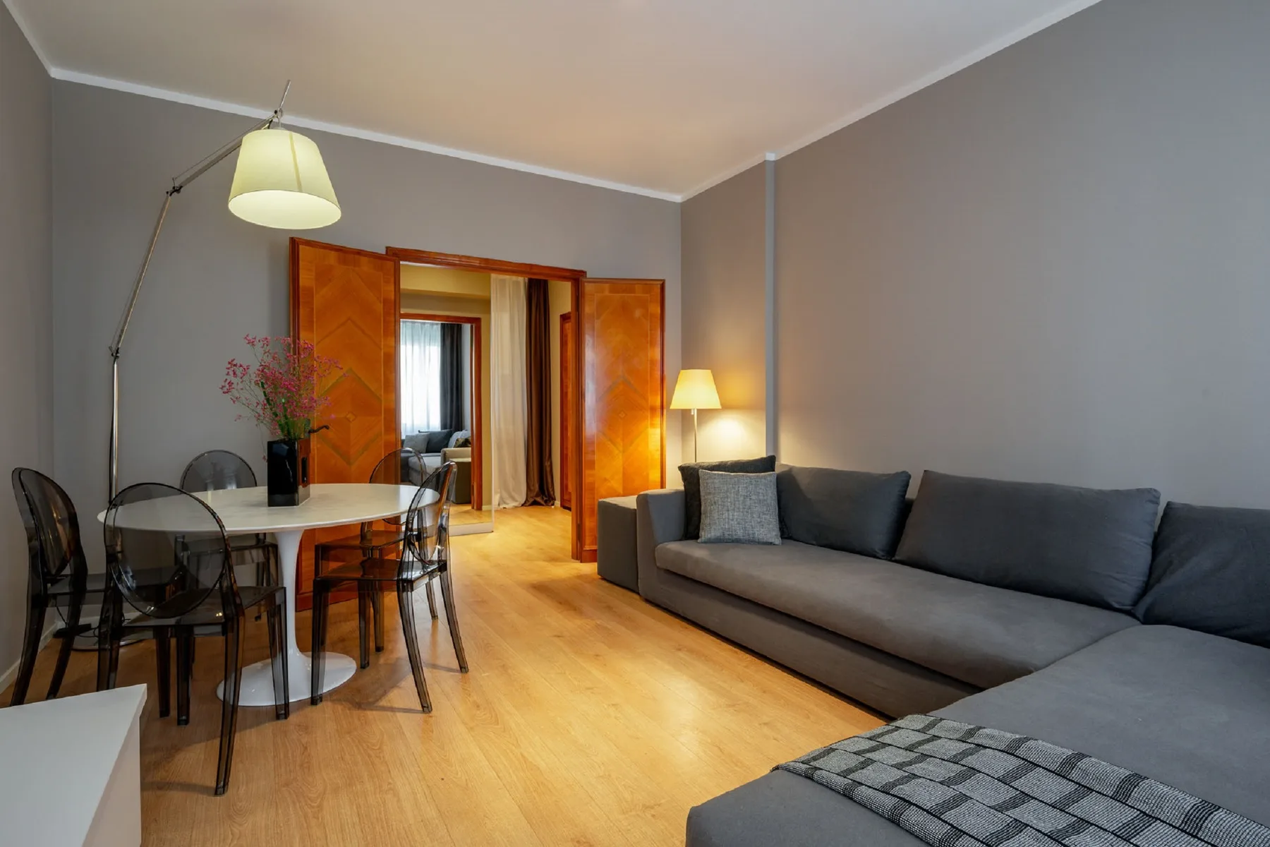 Una sala de estar con asientos grises, una mesa de comedor y suelo de madera.