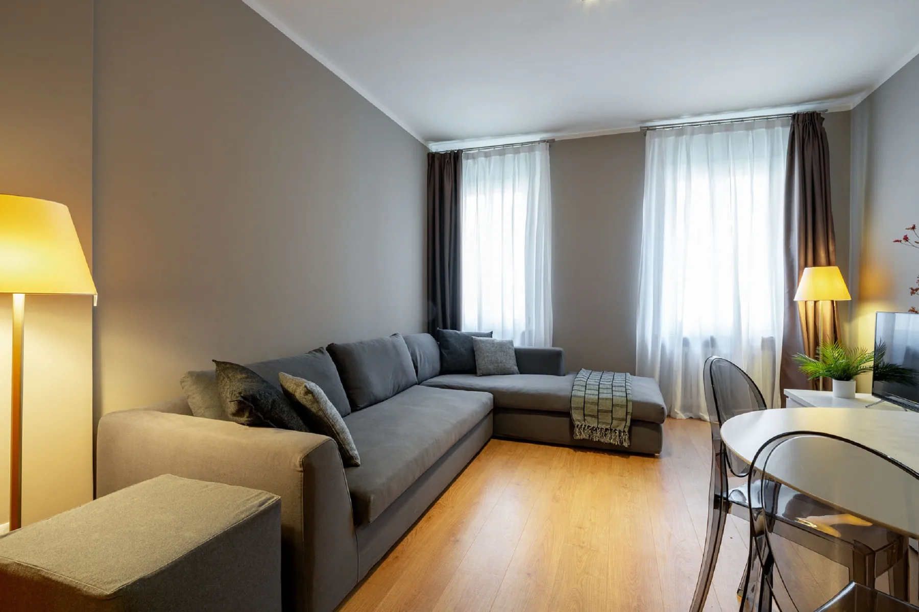 Una sala de estar con asientos en forma de L y ventanas altas con cortinas.