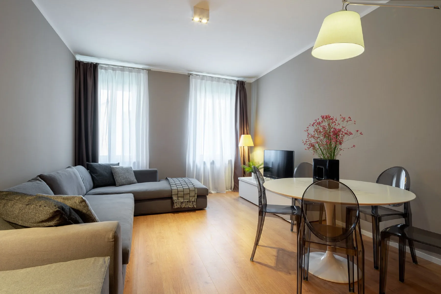 Una sala de estar y comedor con asientos, una mesa y grandes ventanas con cortinas.