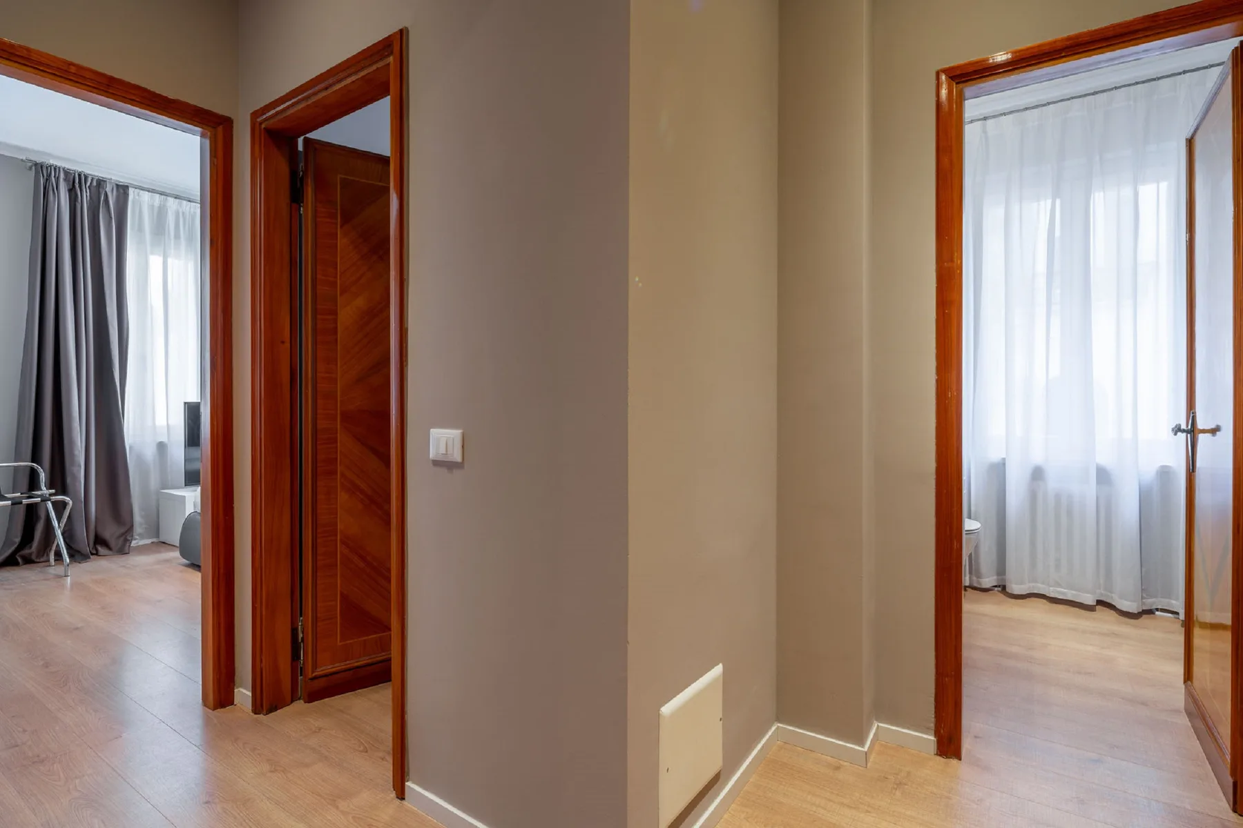 Un pasillo interior conecta dos habitaciones con ventanas con cortinas.