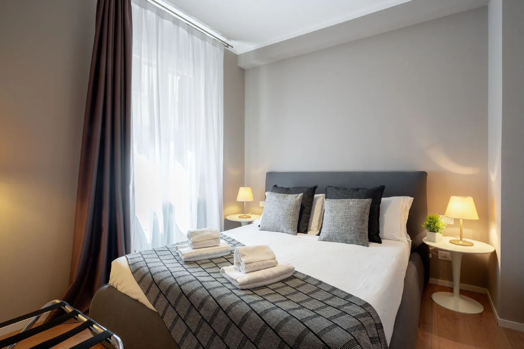 Un dormitorio con una cama bien hecha y una gran ventana con cortinas.