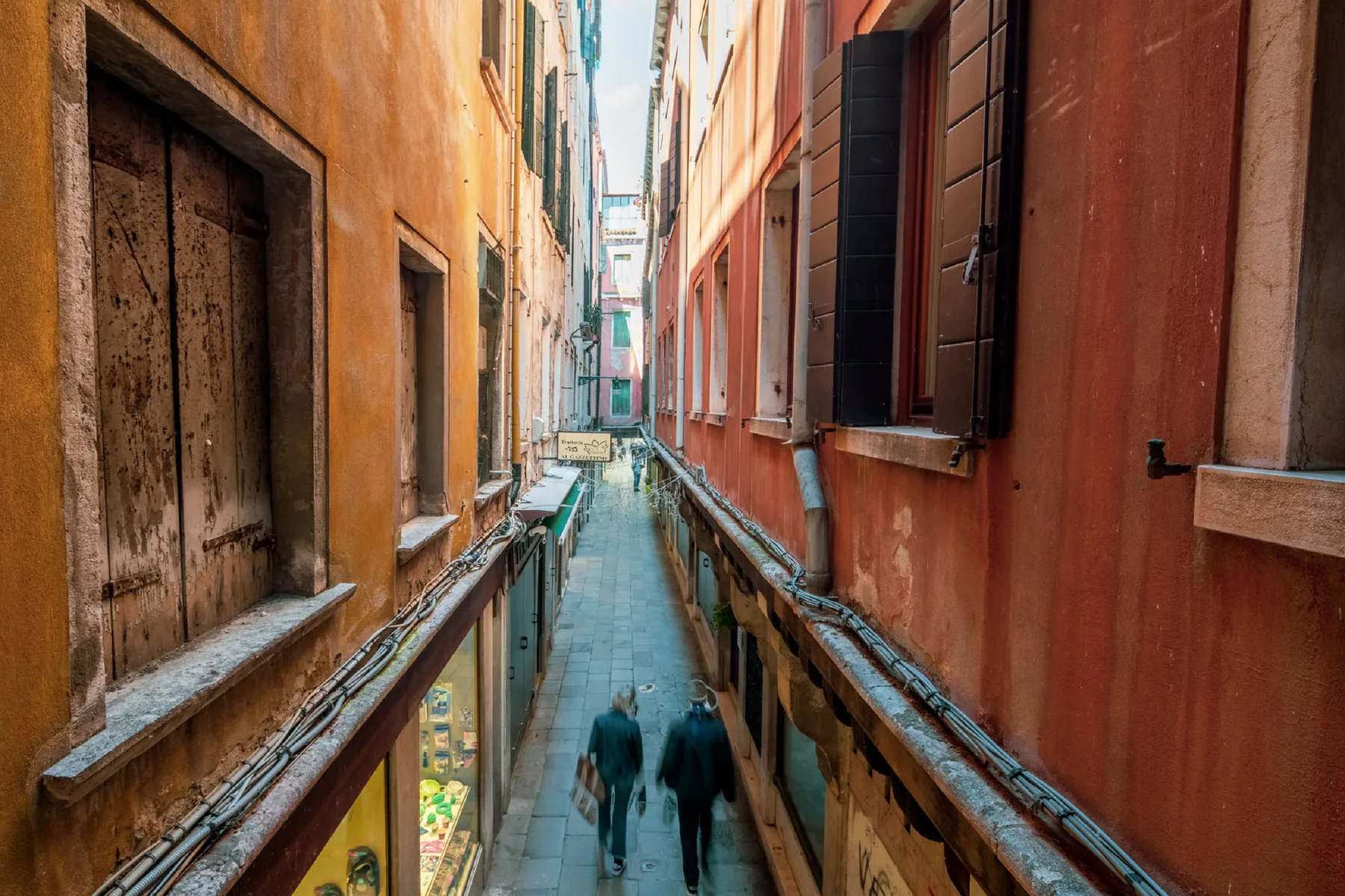 Un estrecho callejón peatonal pasa entre edificios coloridos, con personas caminando.